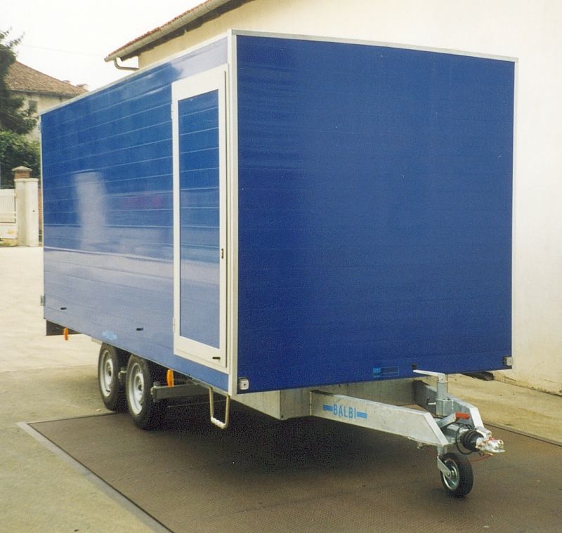 Rimorchio blu chiuso con porta con cornice bianca, su una superficie di cemento.