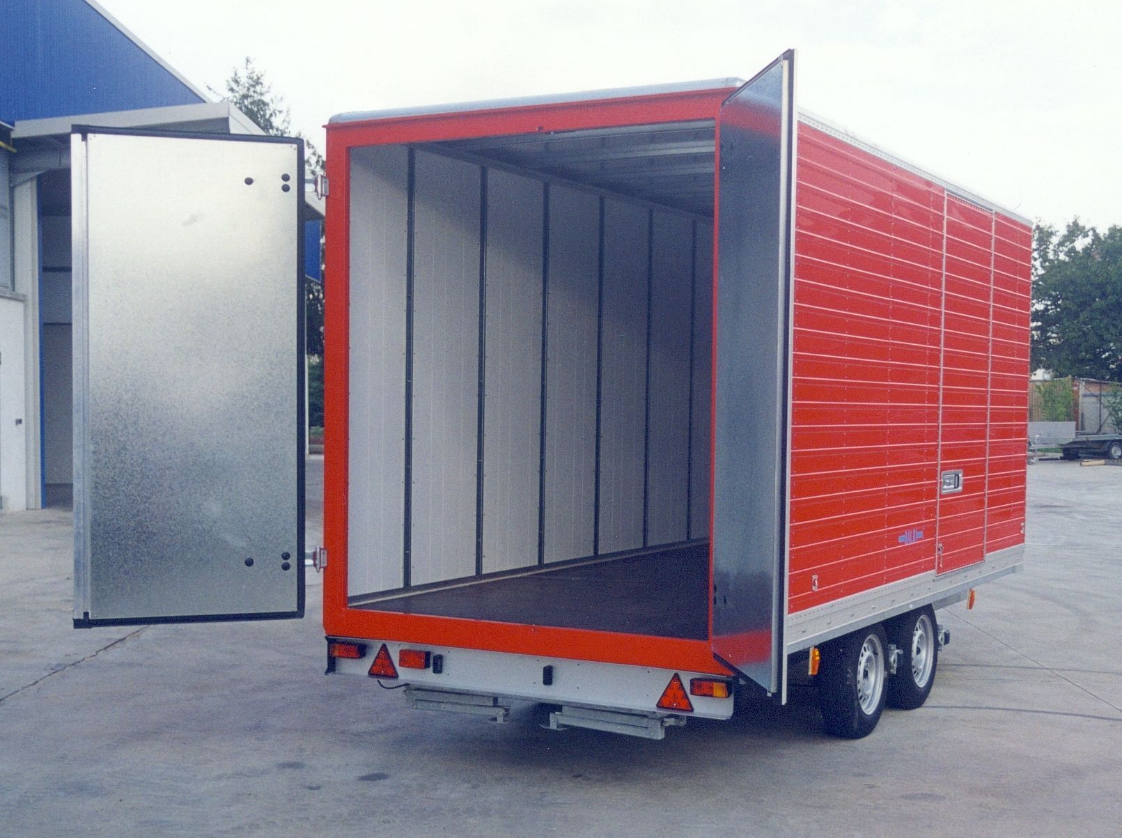 Rimorchio merci rosso e argento con porte aperte; interni con pareti bianche, pavimento nero.