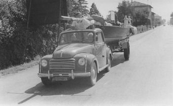 Foto in bianco e nero di un'auto d'epoca che traina un rimorchio su una strada.