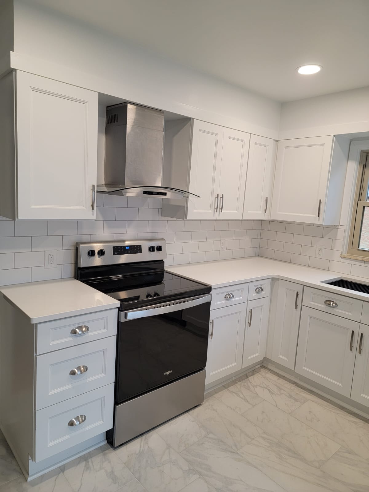 White kitchen with stainless steel appliances, white cabinets, and white tile backsplash.
