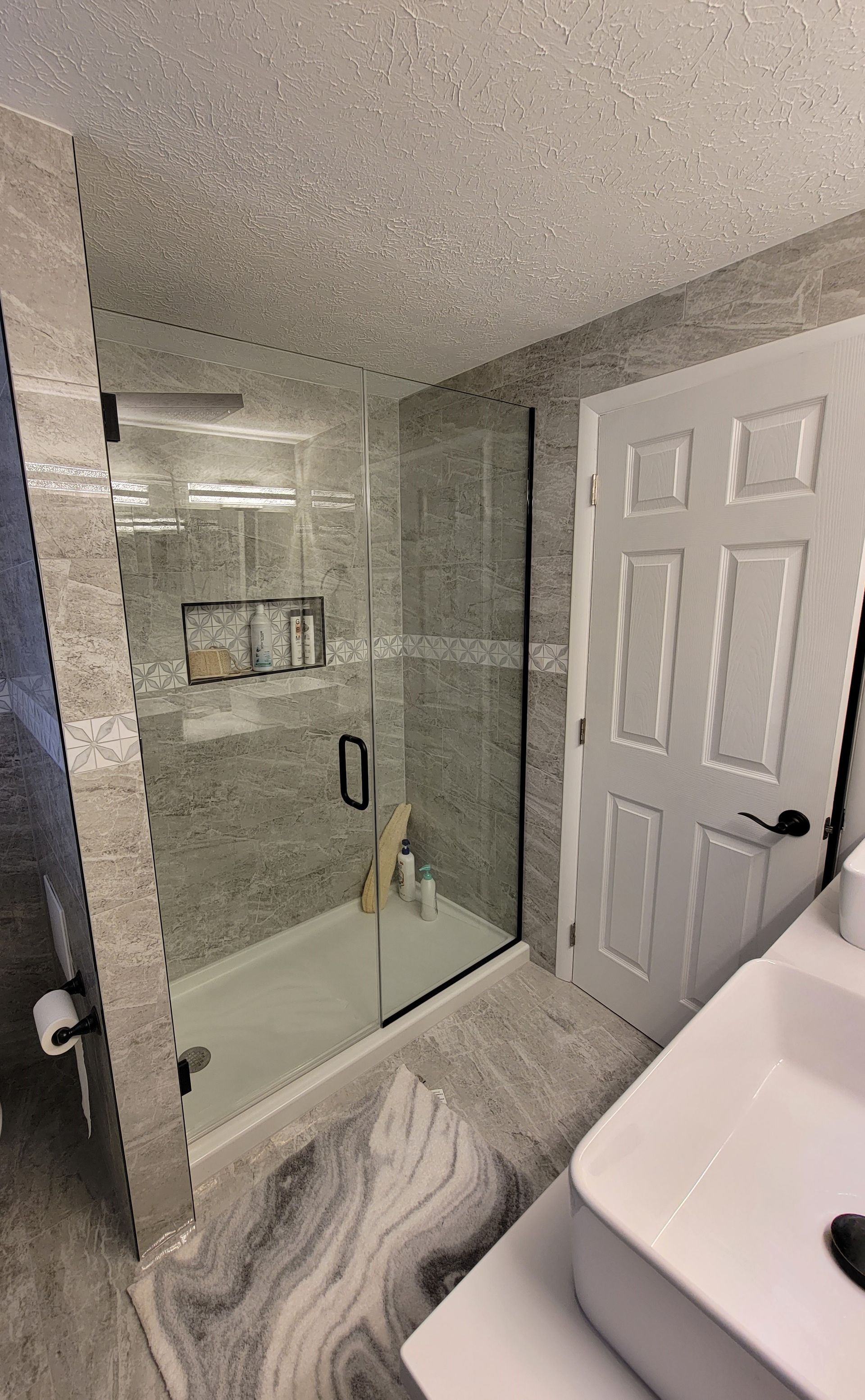 Bathroom with a walk-in shower, gray tiled walls, white door, and a modern sink.