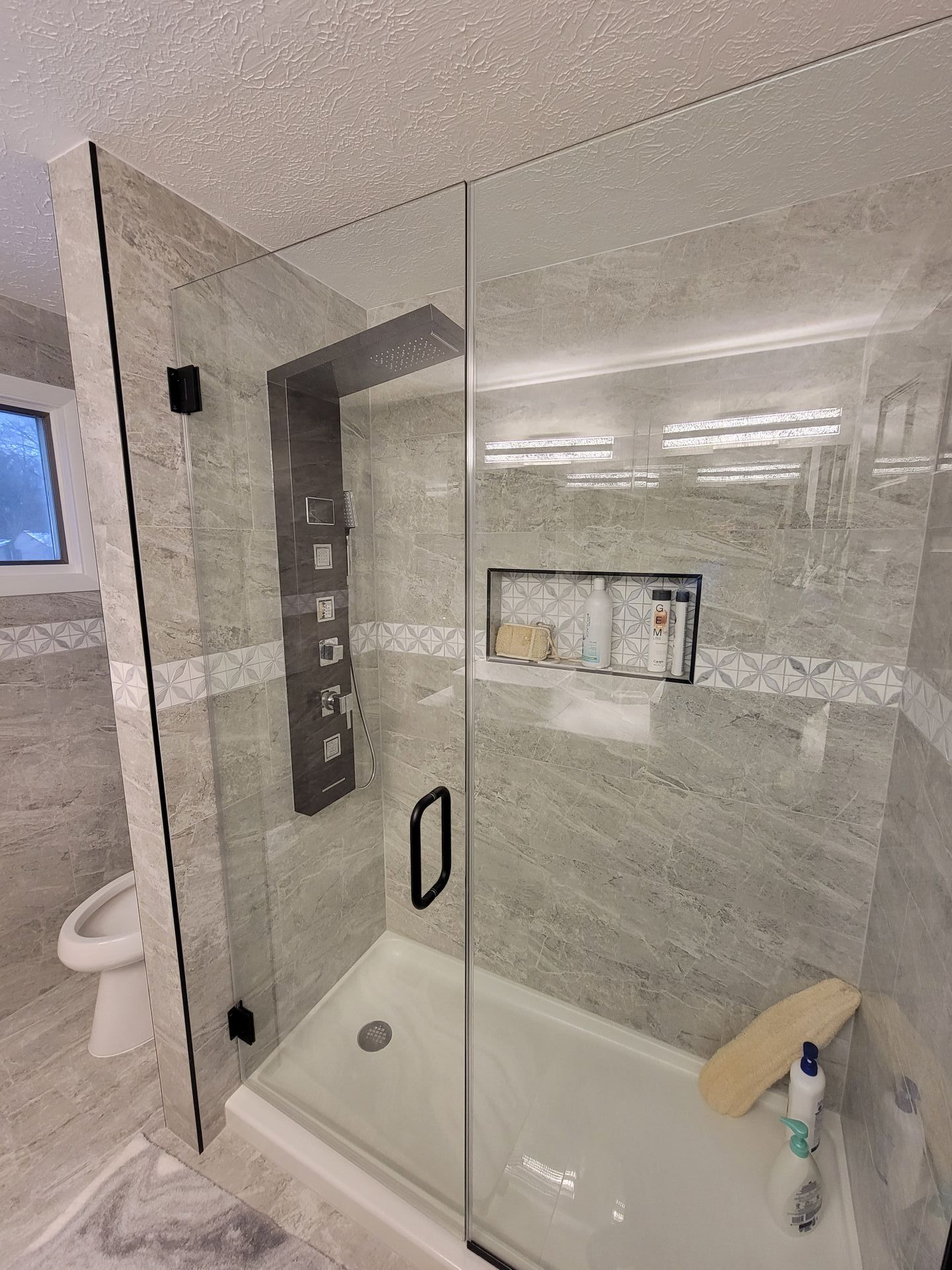 Modern shower with glass doors, gray tile, built-in shelving, and black fixtures.