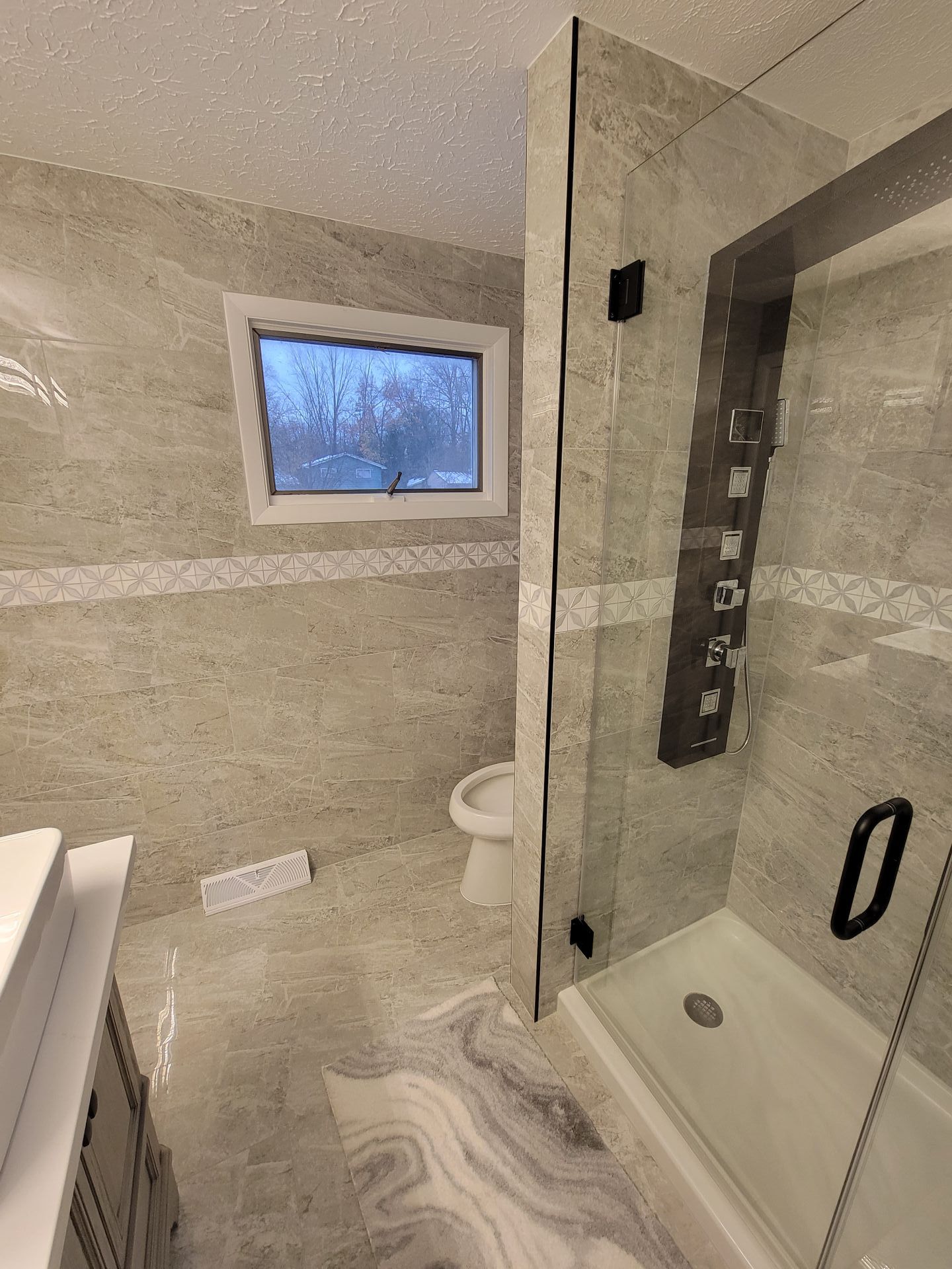 Bathroom with gray tile, shower, toilet, and a small window.