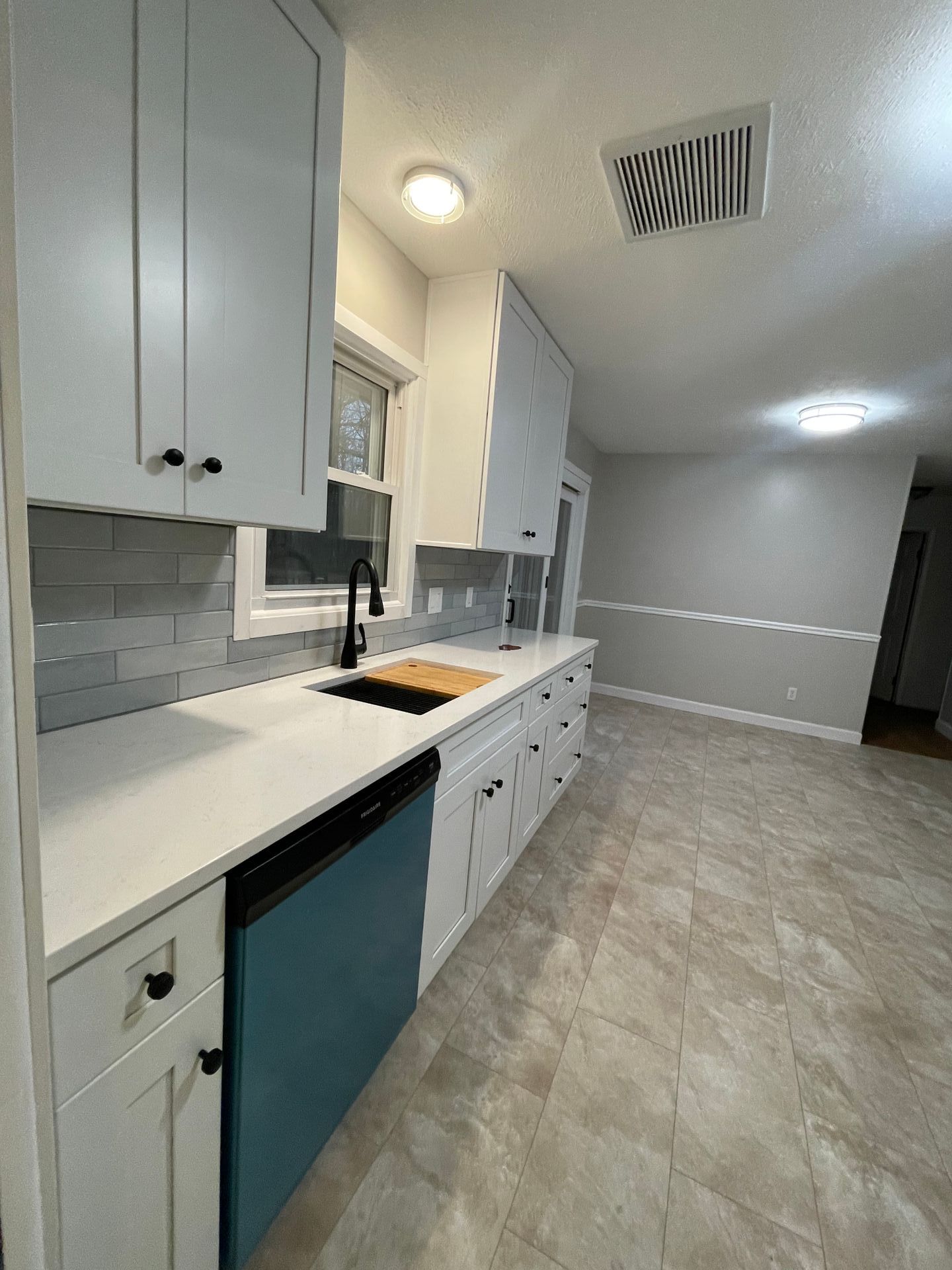 Modern kitchen with white cabinets, teal dishwasher, black faucet, and light countertops.