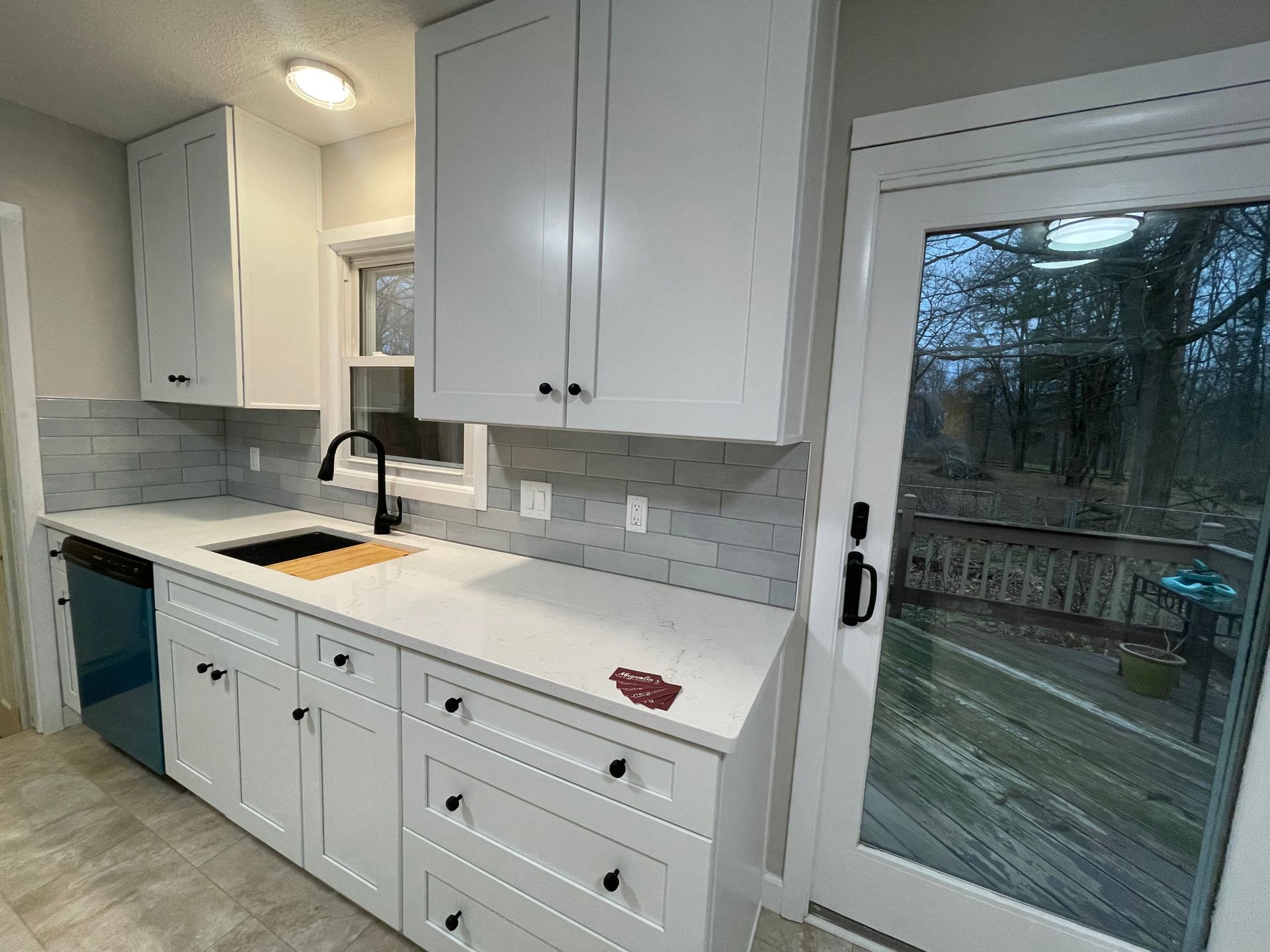 White kitchen cabinets with black hardware and a sliding glass door to a deck.