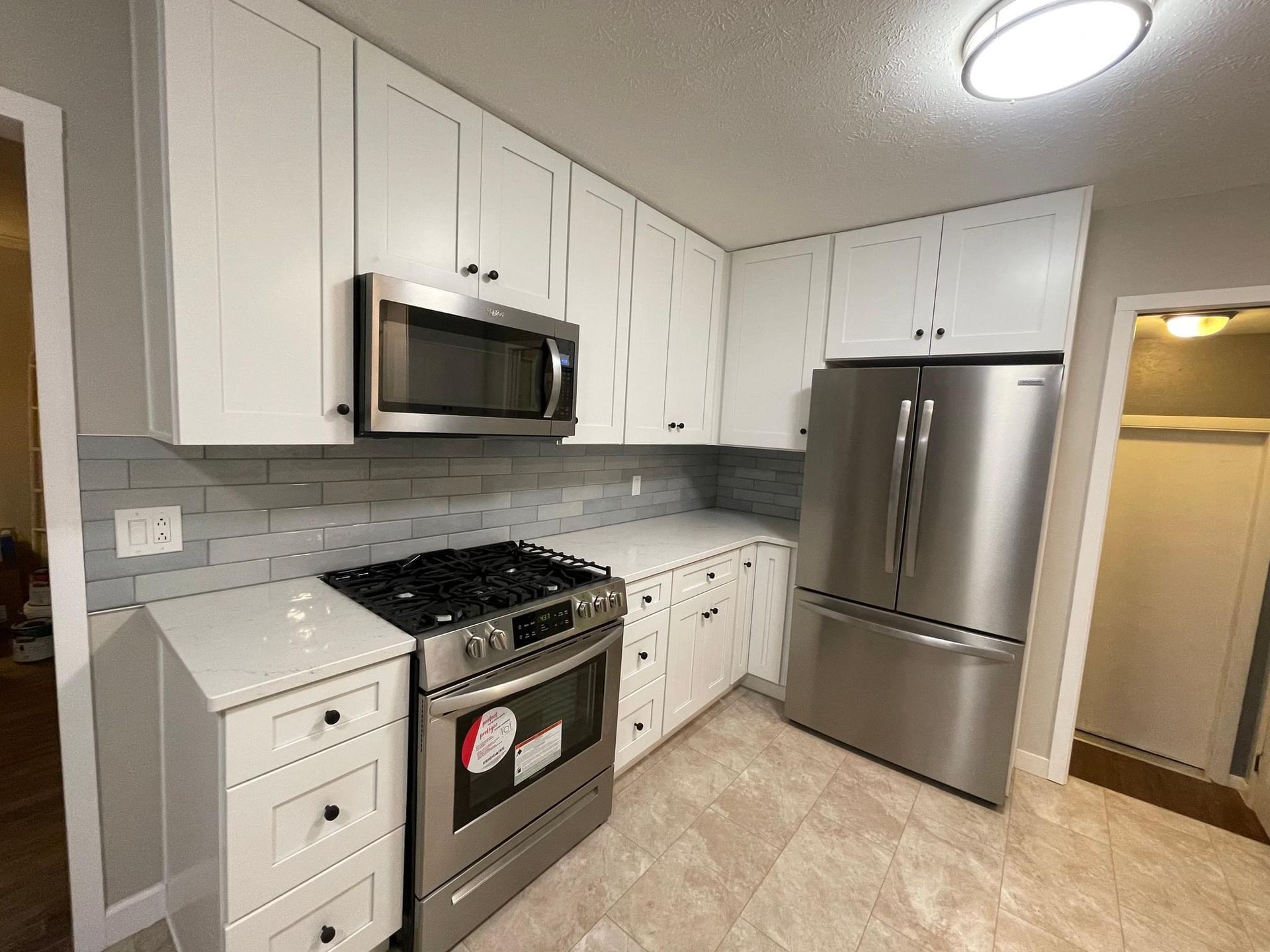 White kitchen with stainless steel appliances, white cabinets, and light gray backsplash.