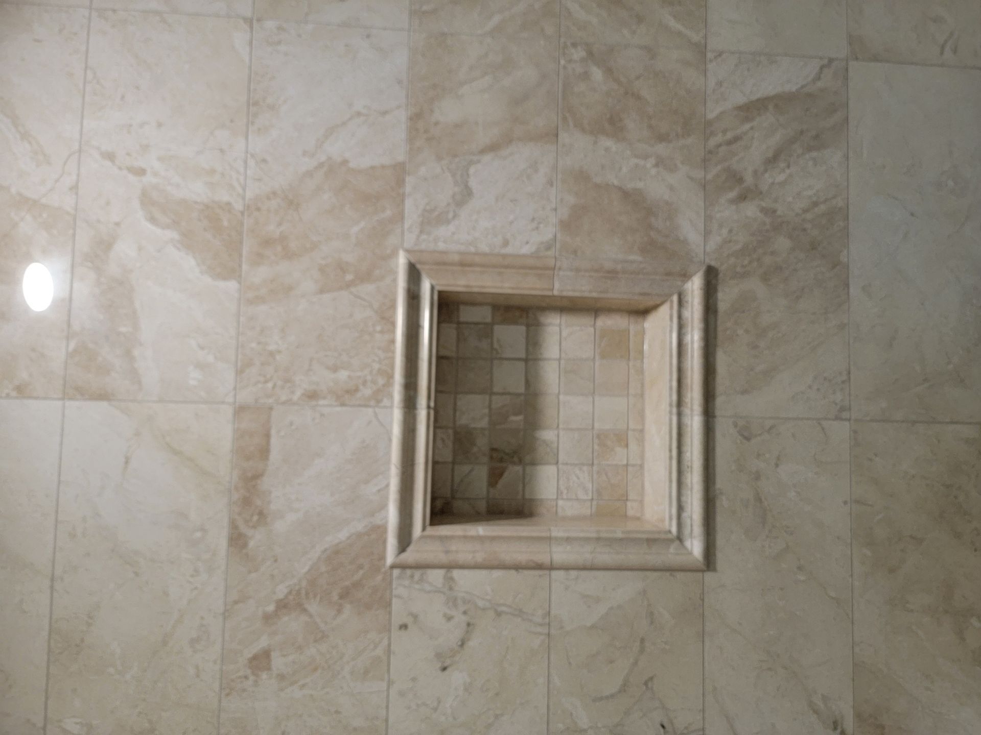 Beige tile wall with a recessed square shelf.