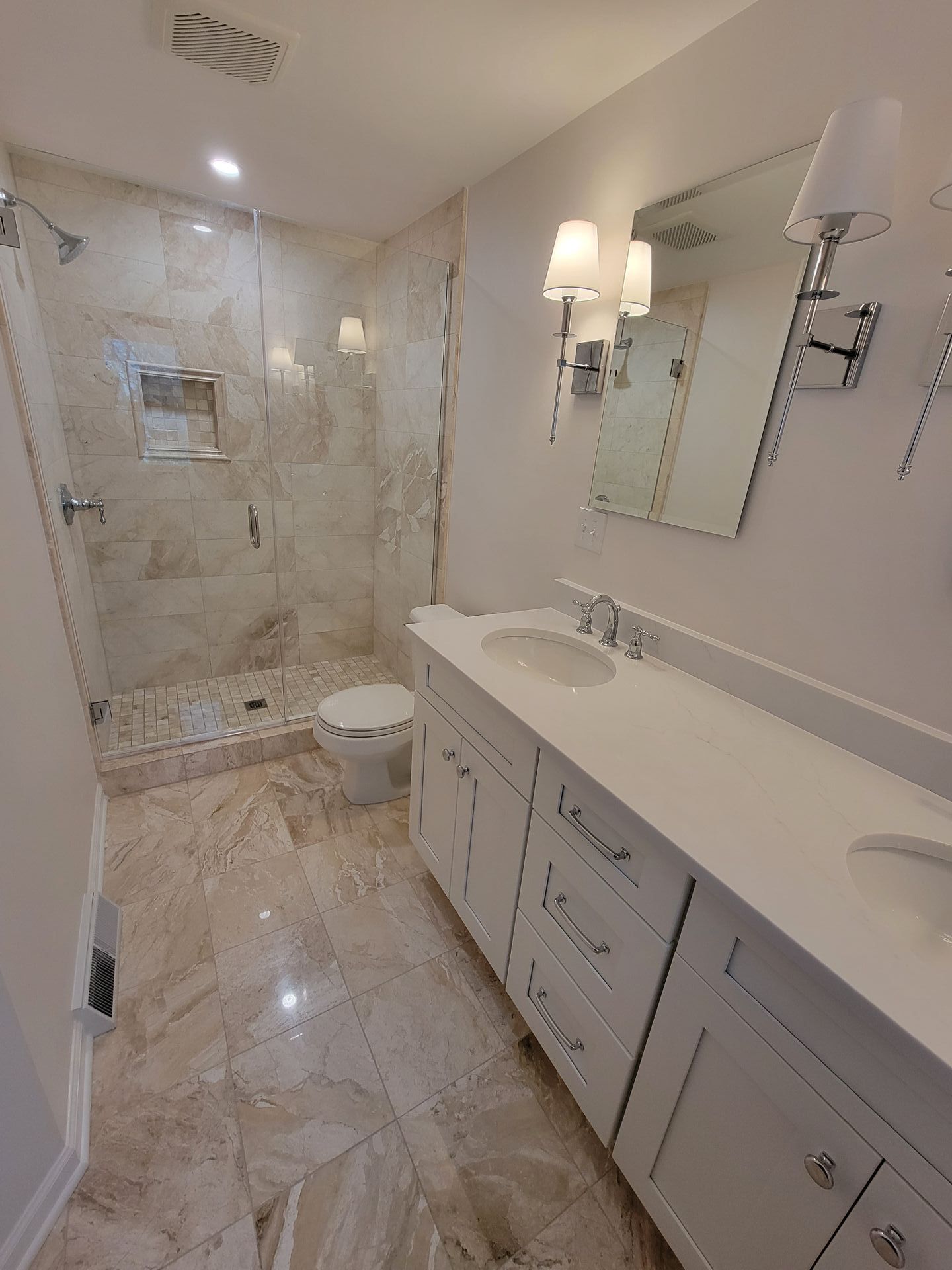 Bathroom with white cabinets, marble tiles, and a glass shower.