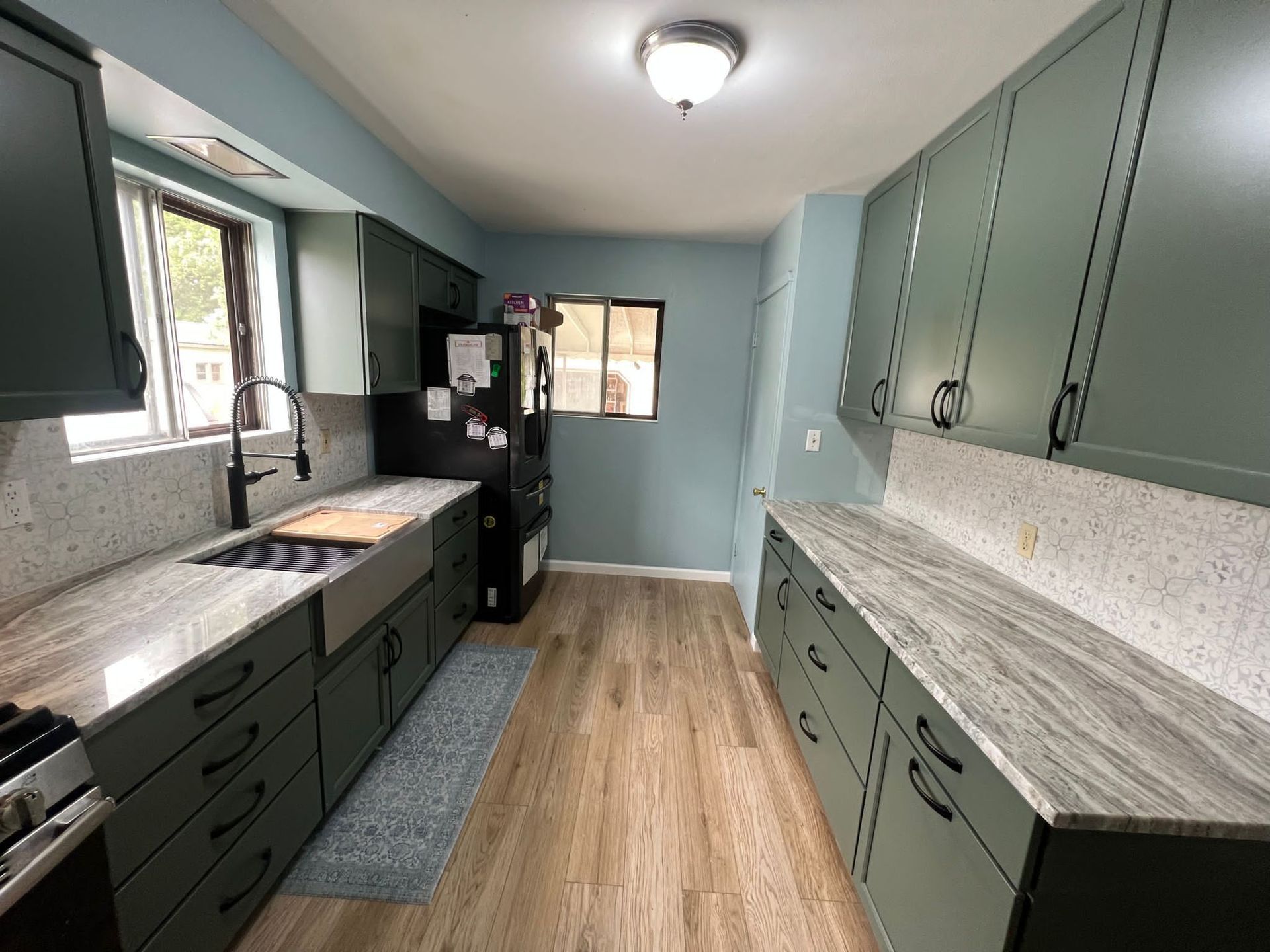 Green kitchen with granite countertops, wooden floor, and a black refrigerator.