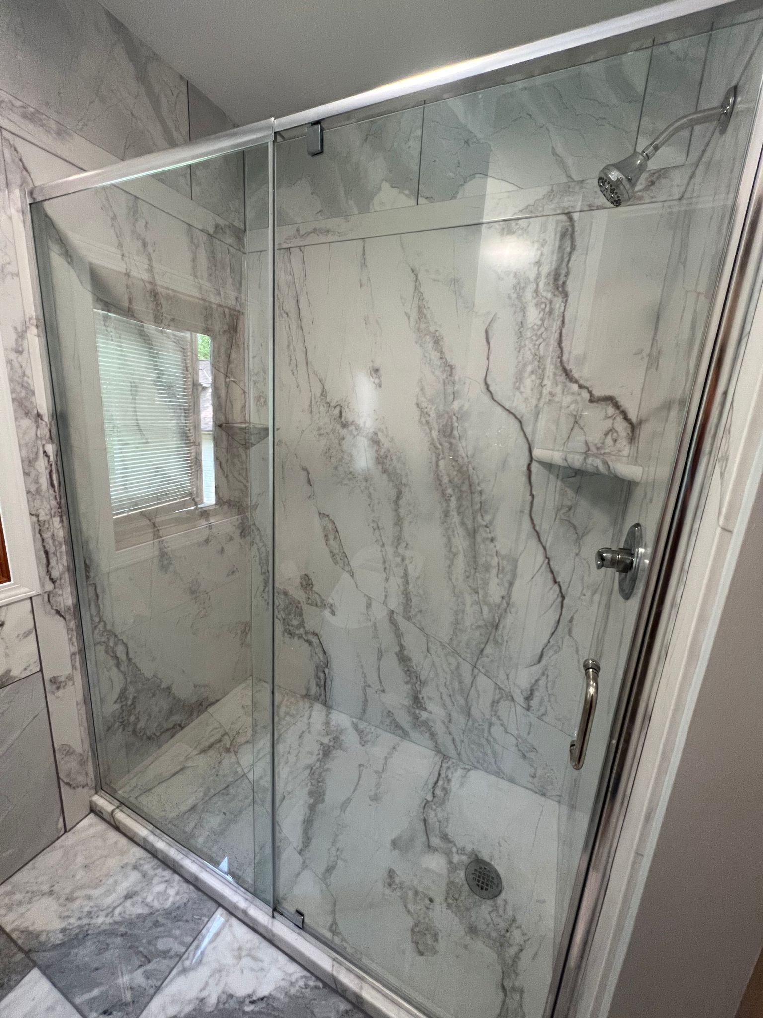 Shower stall with glass doors, marble-patterned walls and floor, and silver hardware.