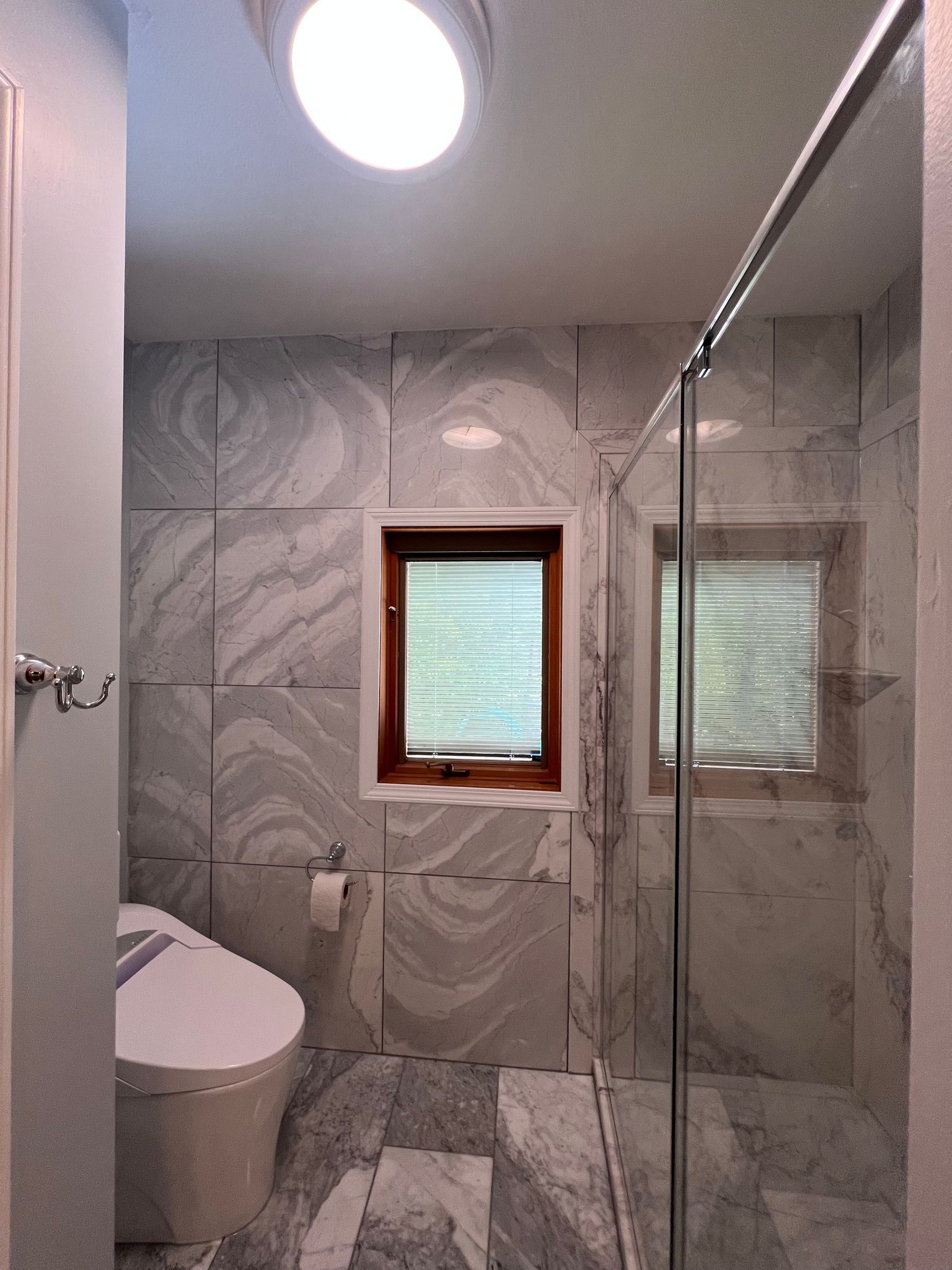 Bathroom with marble tile walls, window, toilet, and glass shower door.