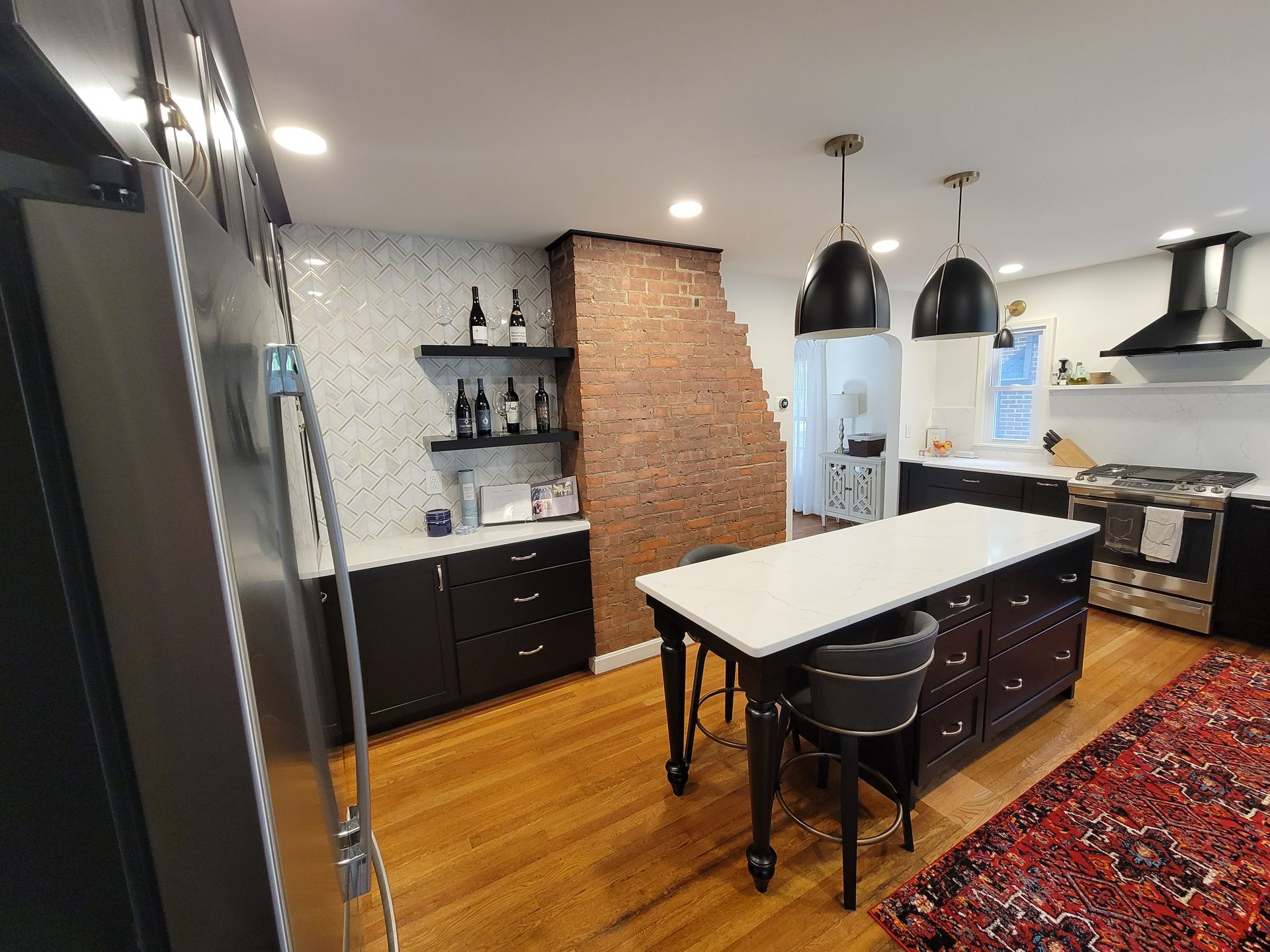 Kitchen with dark cabinets, brick accent wall, island, hardwood floors, and overhead pendant lights.