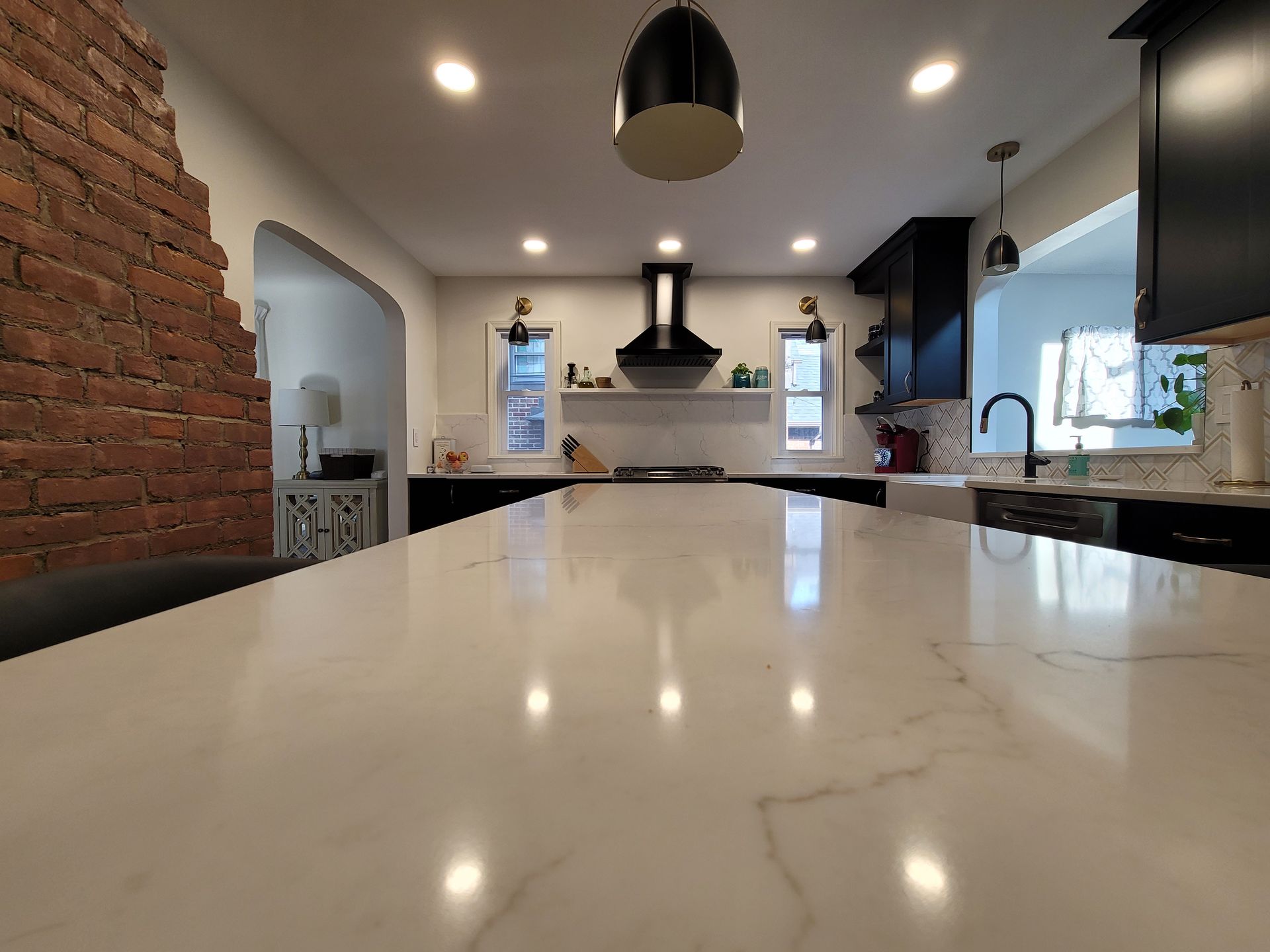 Kitchen with white countertop, exposed brick wall, black cabinets, and stainless steel appliances.