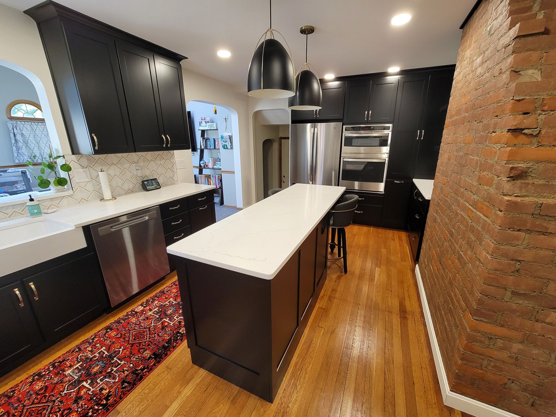 Kitchen with dark cabinets, white countertops, stainless steel appliances, and a red rug.