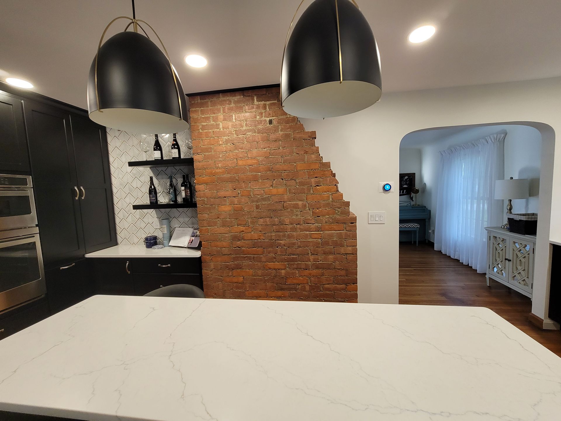 Kitchen with exposed brick wall, black cabinets, white countertop, and hanging black pendant lights.