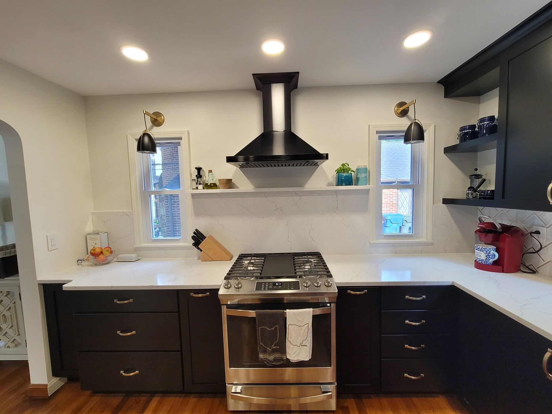 Modern kitchen with black cabinets, white countertops, stainless steel stove, and a black range hood.