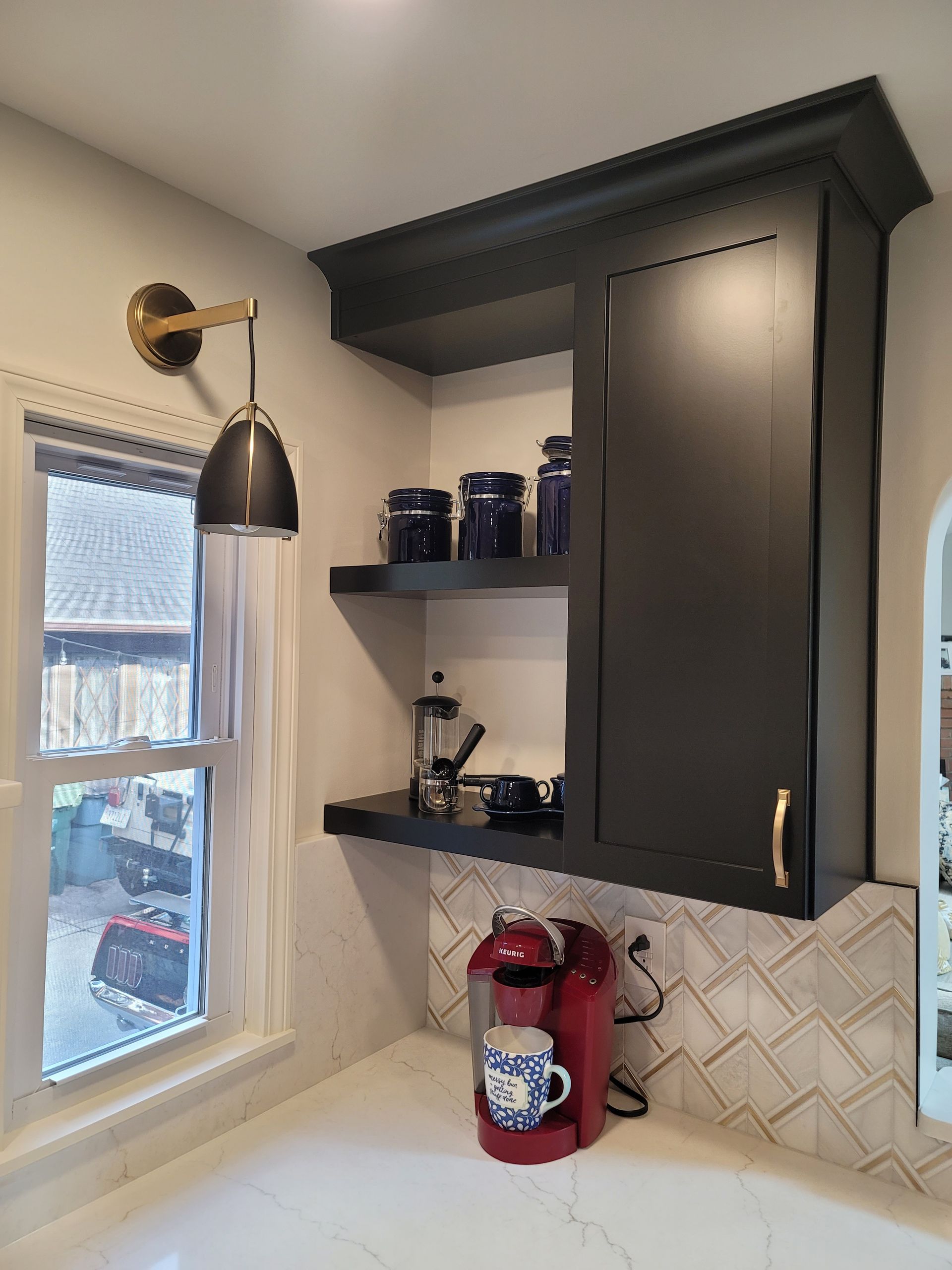 Dark cabinetry coffee station with open shelves and a red coffee maker near a window.