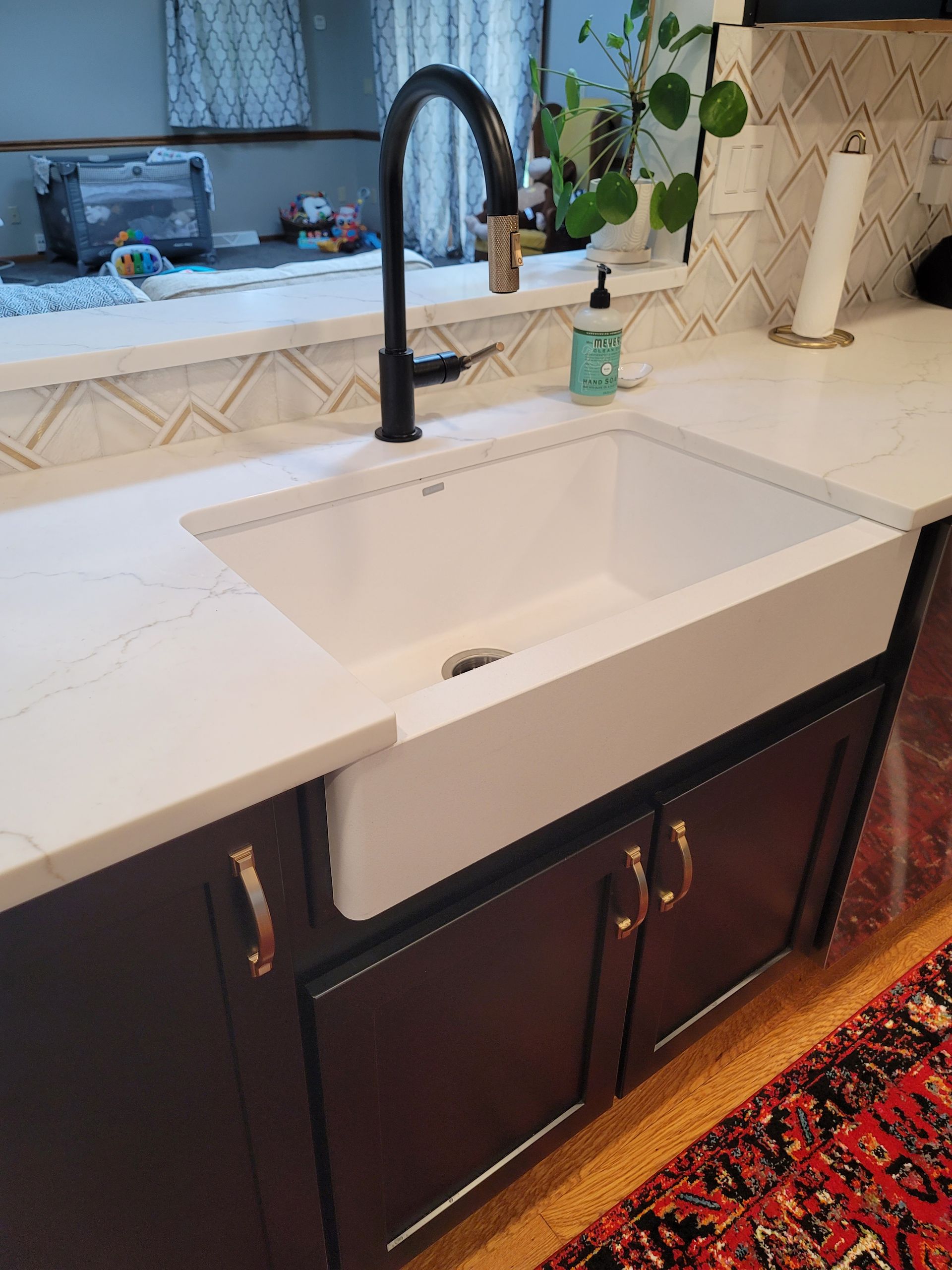 White farmhouse kitchen sink with black faucet, dark cabinets, and white countertop.