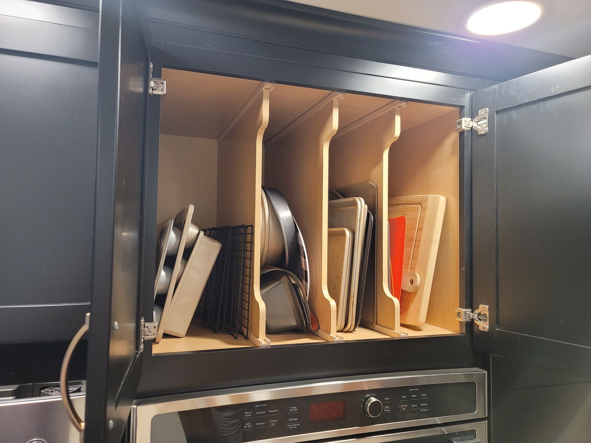 Cabinet with dividers storing baking sheets, pans, and cutting boards. Black cabinet, light-colored dividers.