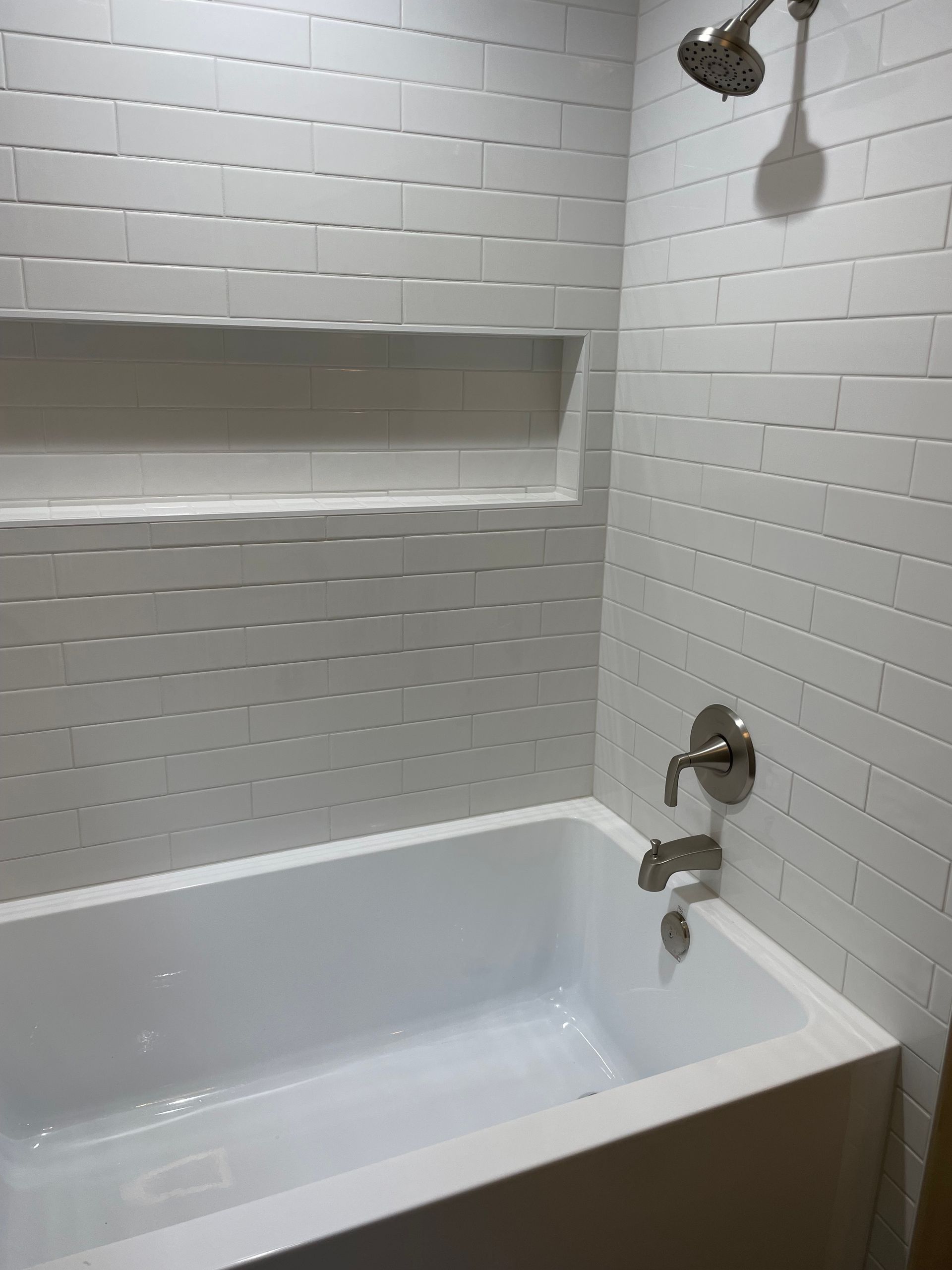 White tiled shower with built-in shelf and bathtub; showerhead and faucet visible.