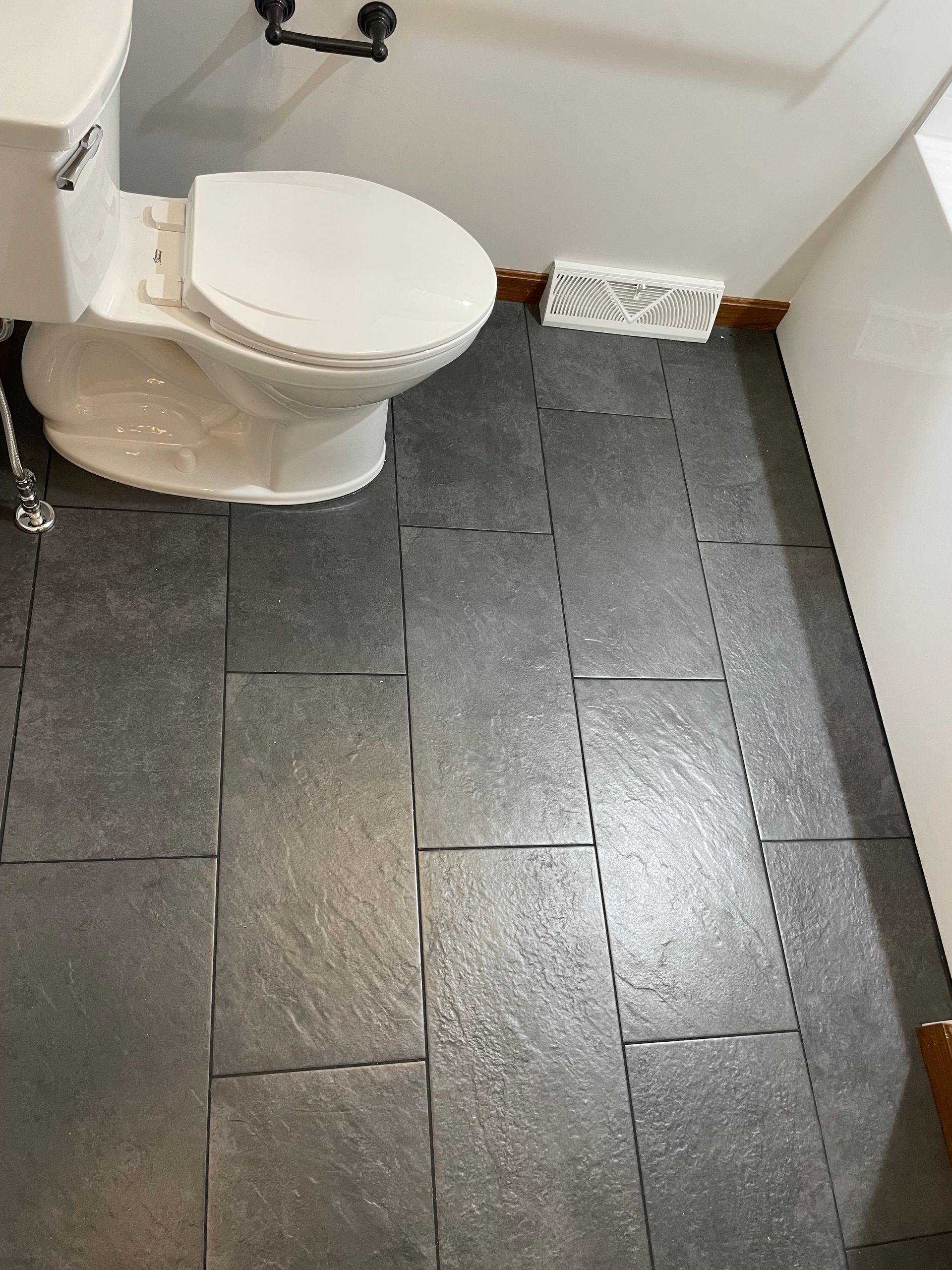 A toilet in a bathroom with dark gray tiled floor. The toilet is white.