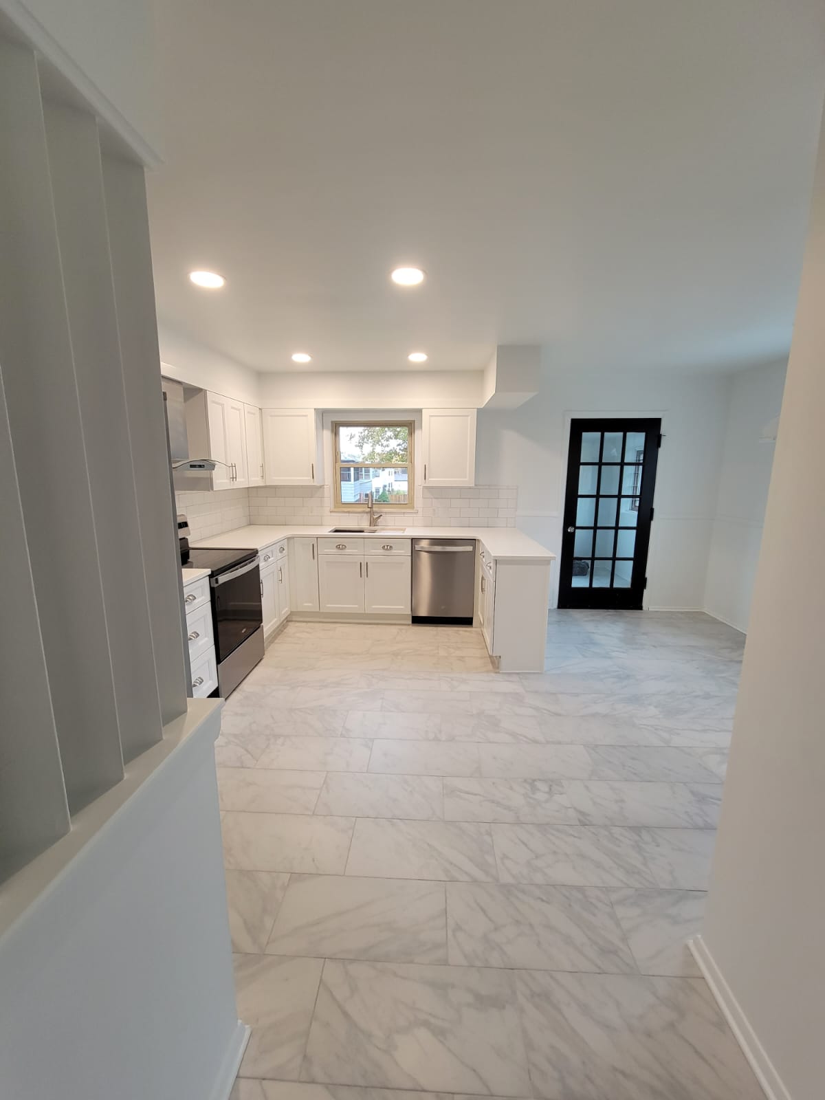 Bright, modern kitchen with white cabinets, countertops, stainless steel appliances, and marble-look flooring.