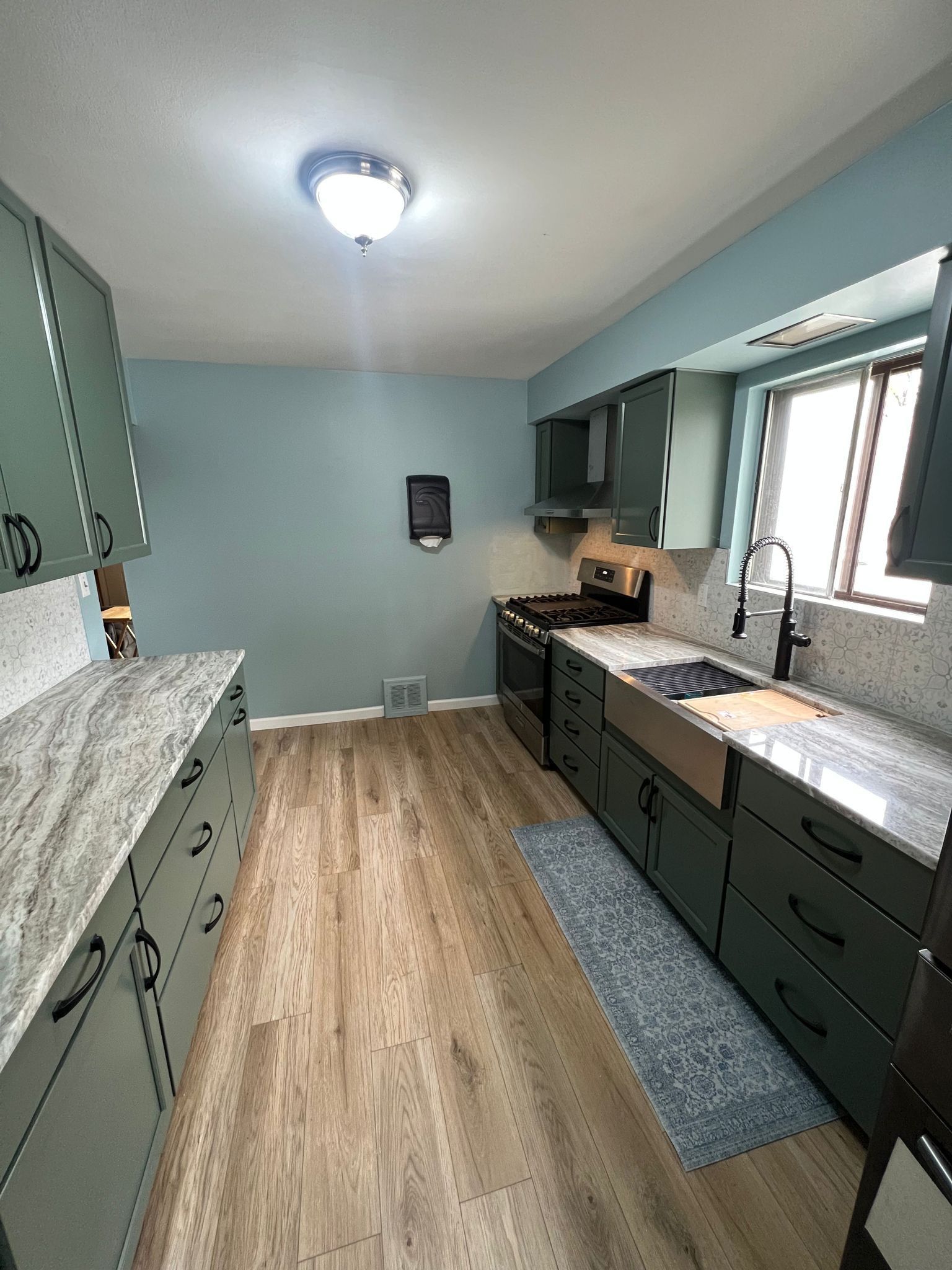 Kitchen with green cabinets, light countertops, and wooden floors.