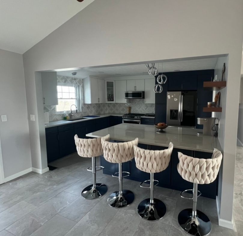 Modern kitchen with navy and white cabinets, island with four beige bar stools, gray countertops and flooring.