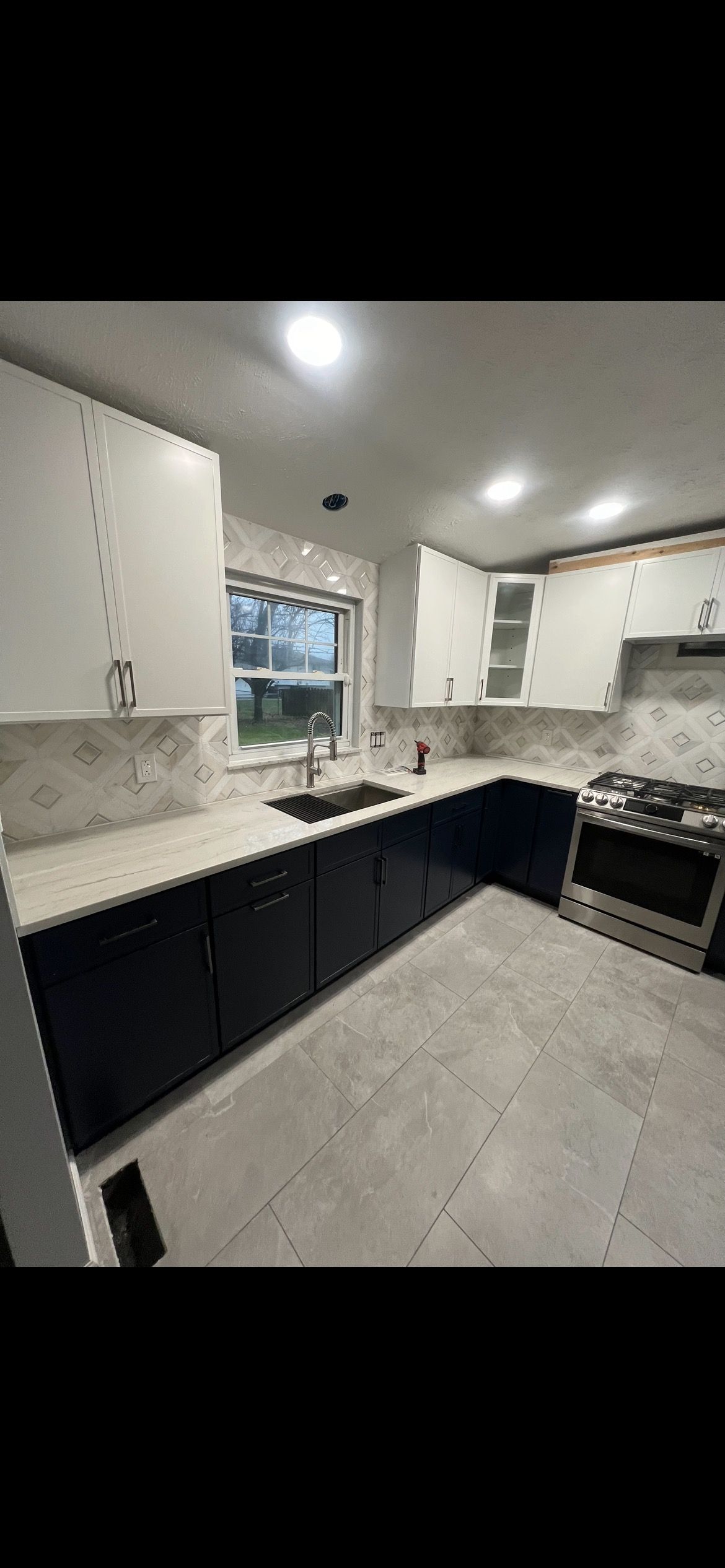 Modern kitchen with white upper cabinets and navy blue lower cabinets, light countertops, and a stainless steel stove.