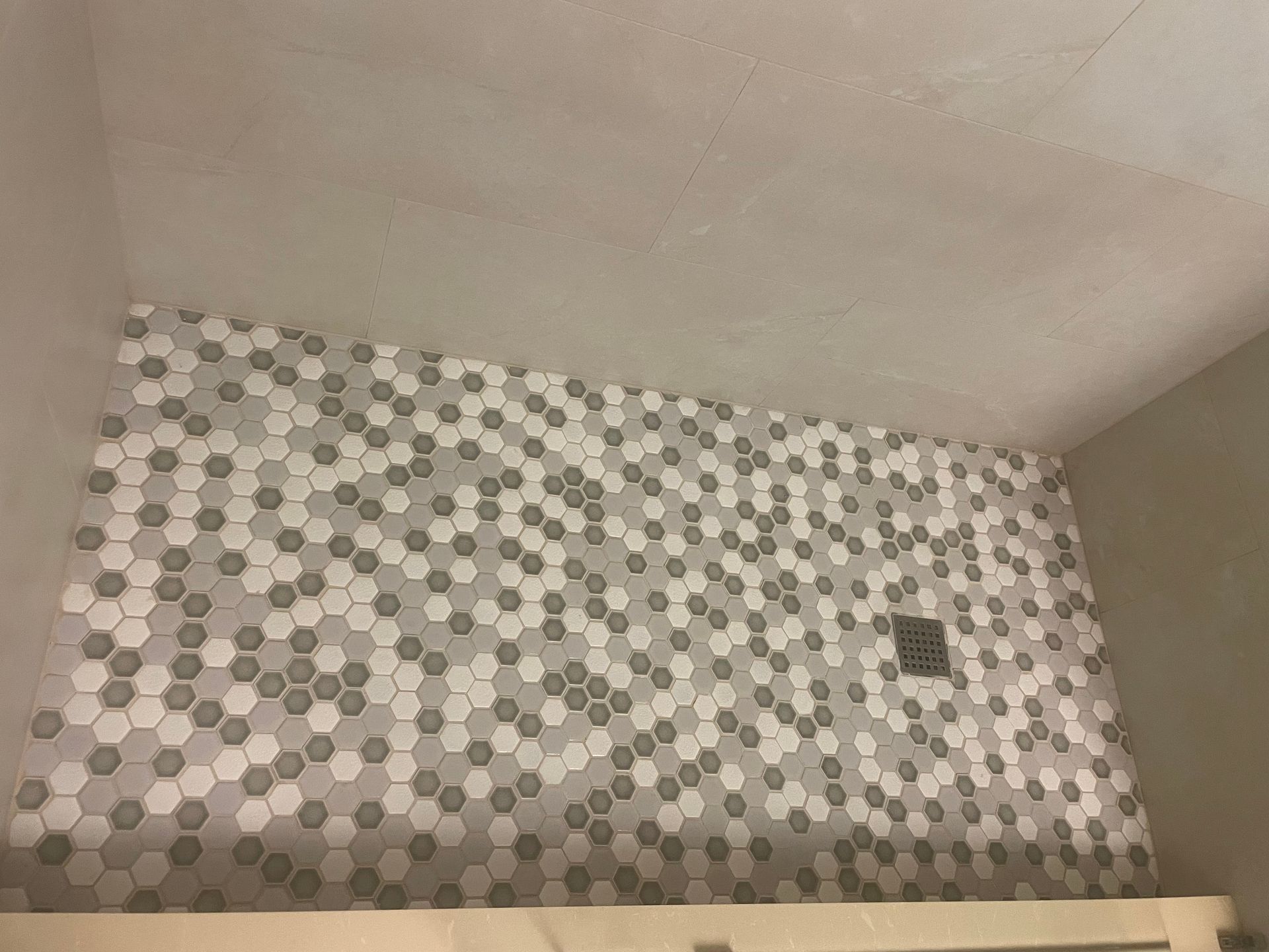 Hexagon tile shower wall, gray and white, above a ledge, under a plain ceiling.