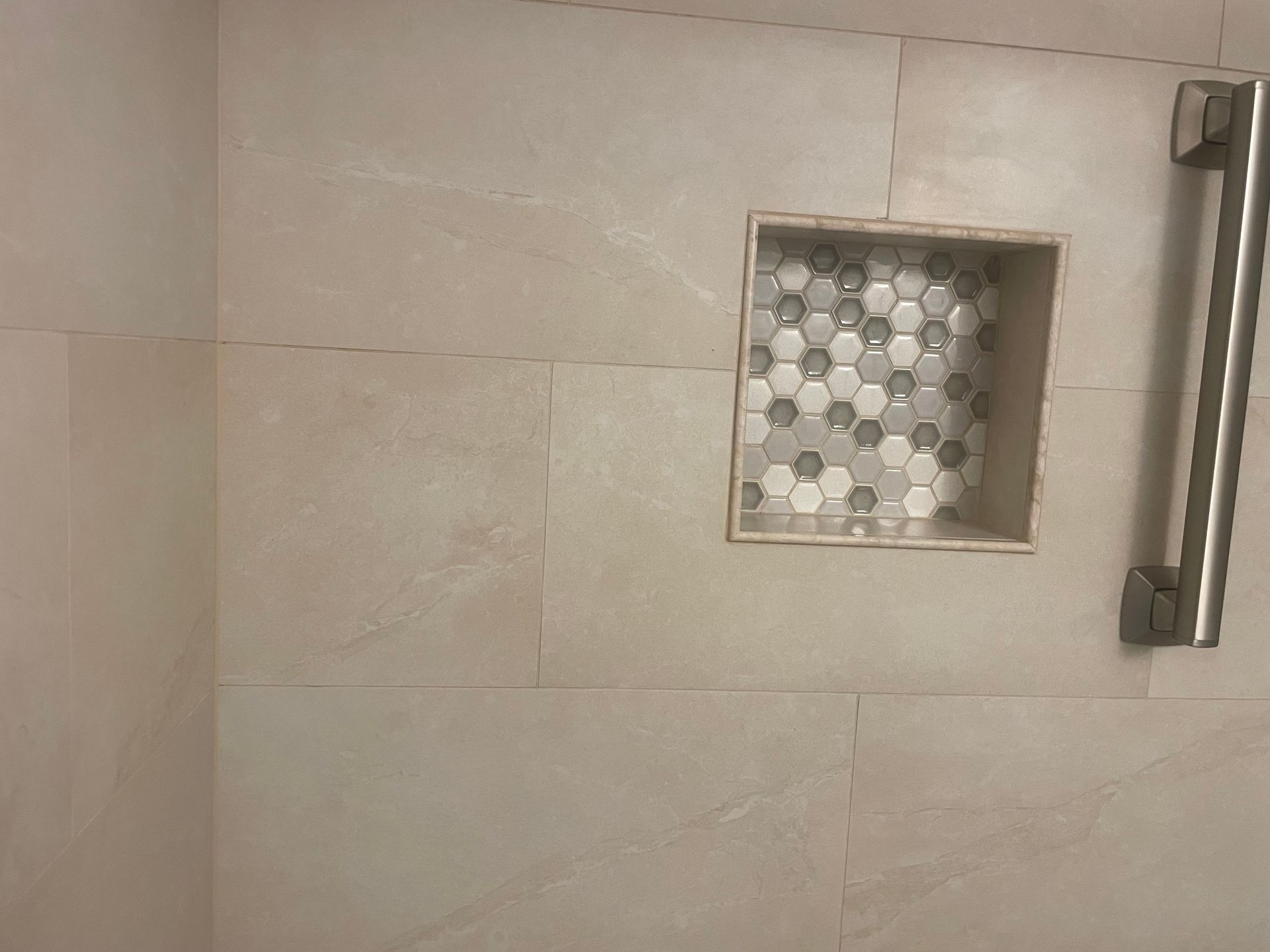 Shower wall with built-in shelf, hexagon tile inside, and a stainless steel grab bar. Beige tiles.