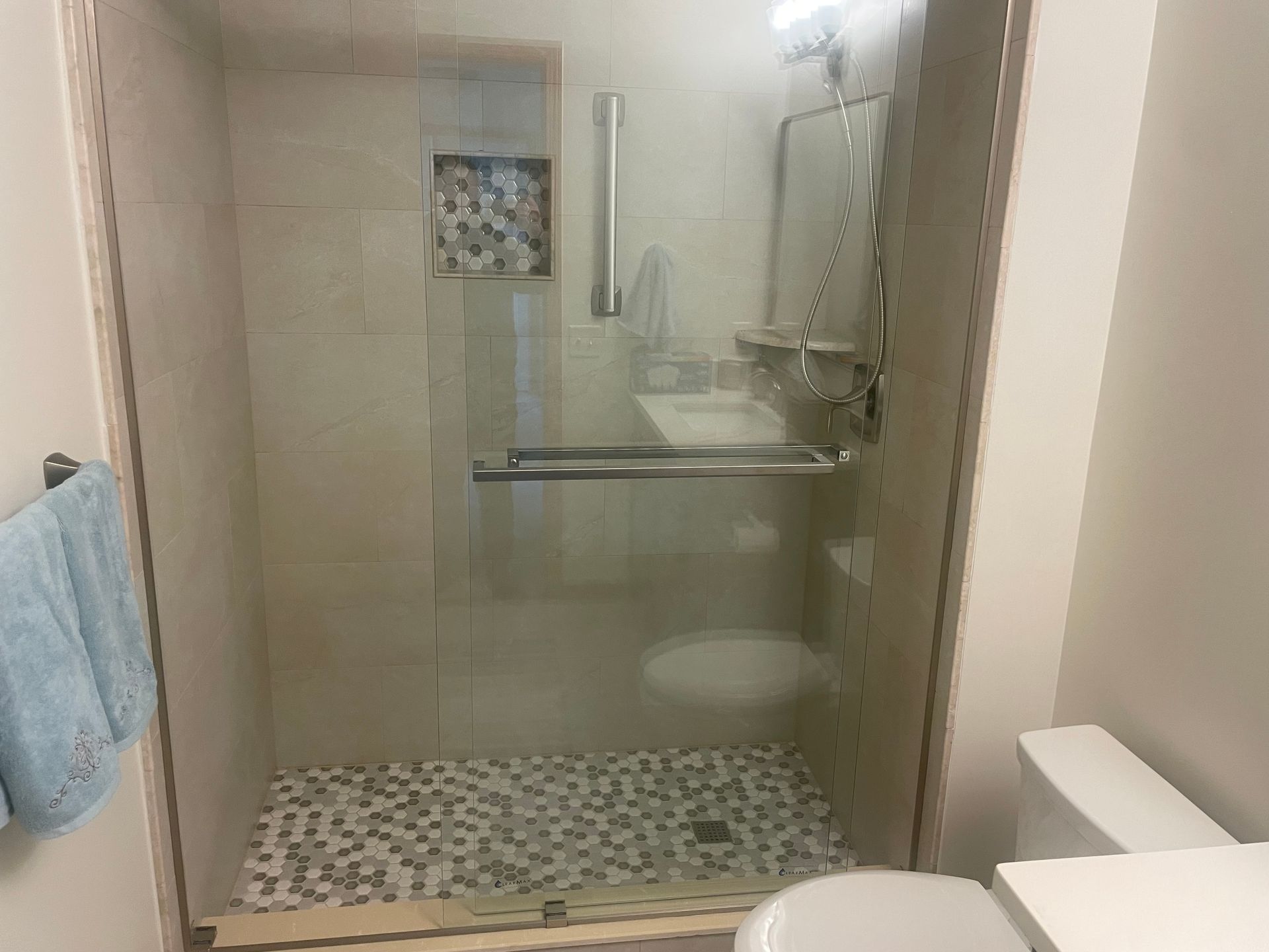 Shower stall with glass door, stone floor, built-in shelf, grab bar, and recessed niche.