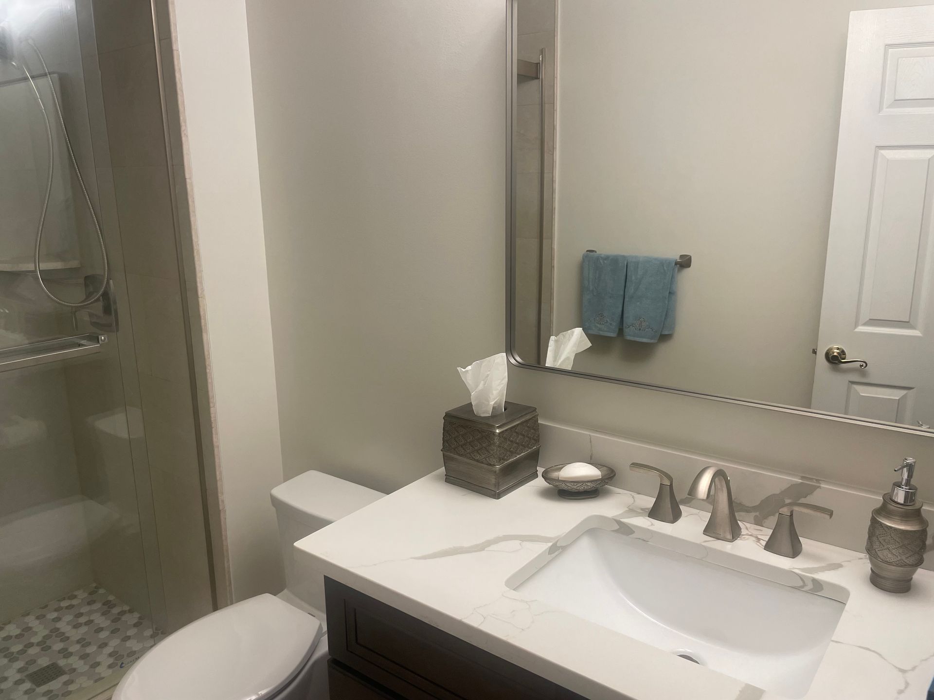 Bathroom with white sink, toilet, and shower, light gray walls, and blue towel.
