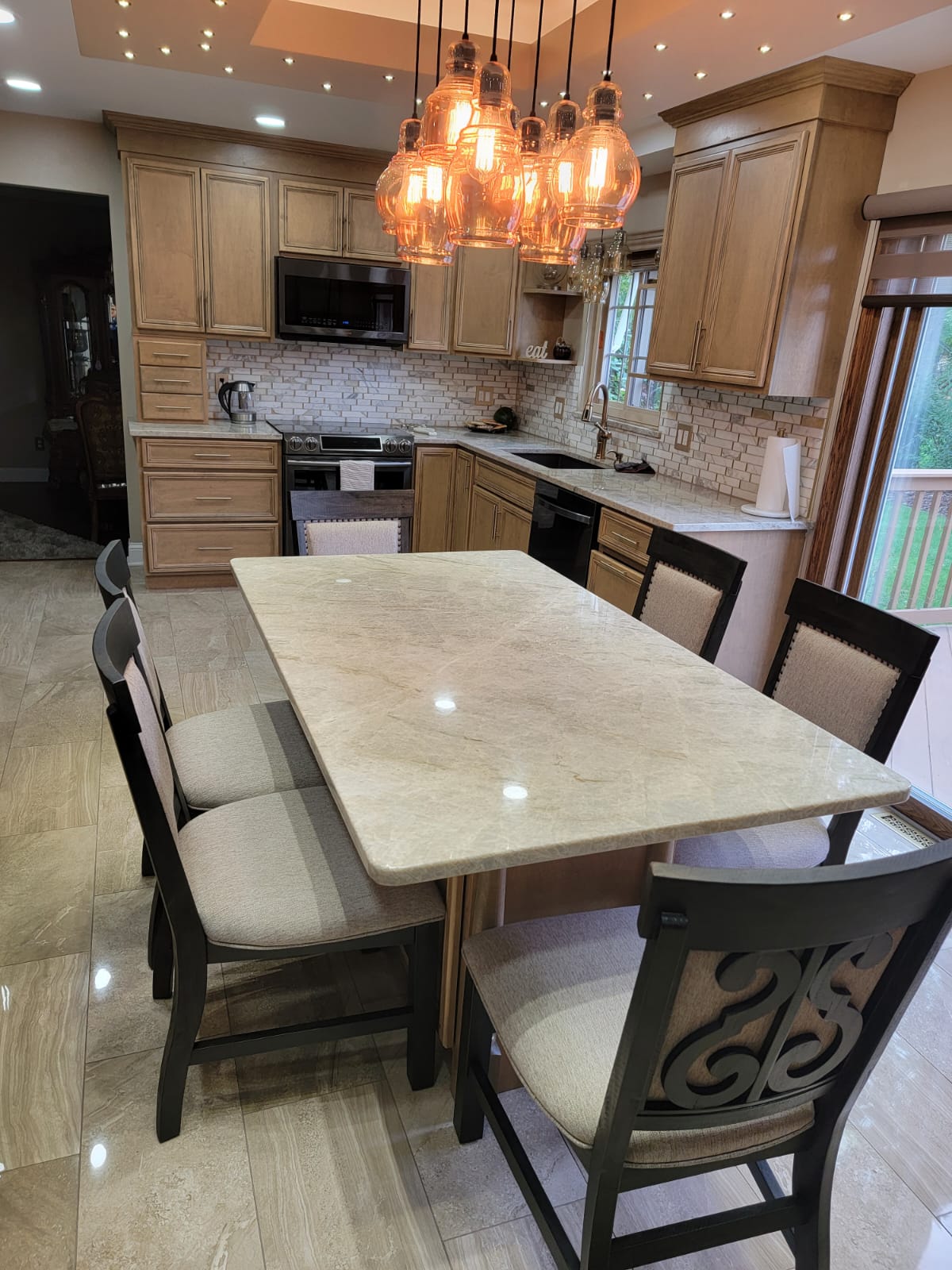 Kitchen with beige cabinets, marble countertop, dining table, and pendant lights.