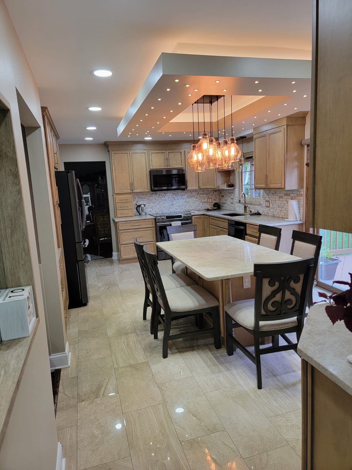 Kitchen with light wood cabinets, marble island with seating, pendant lights, and recessed ceiling lights.
