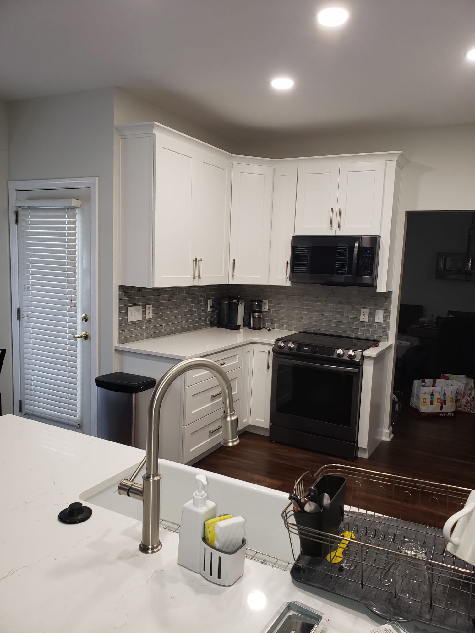 Modern kitchen with white cabinets, stainless steel sink, black appliances, and white countertop.