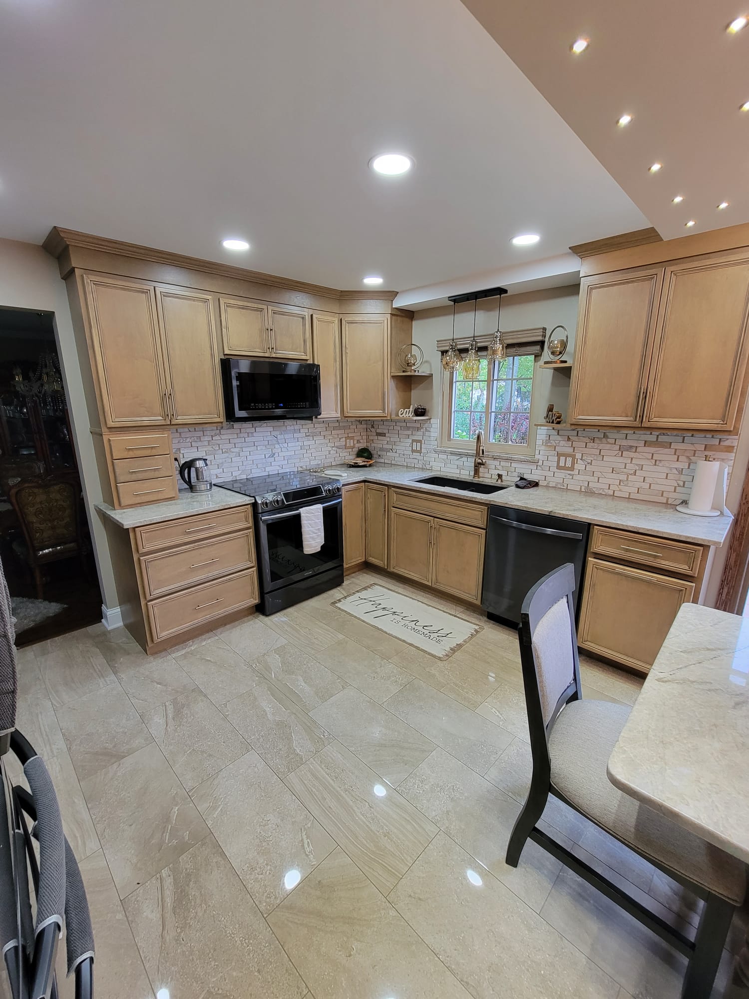 Kitchen with light wood cabinets, black appliances, and marble backsplash.