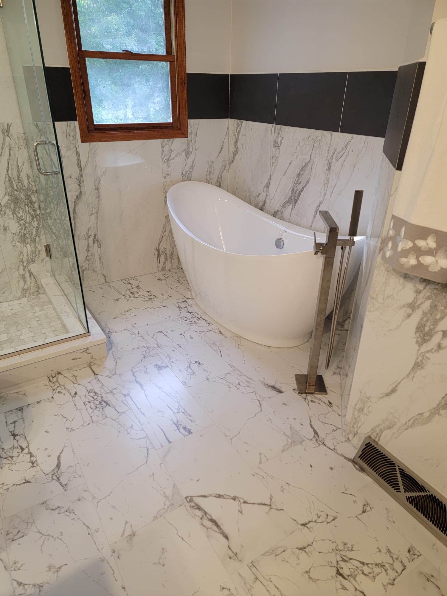 Bathroom with white marble tile, a freestanding tub, and a glass shower.