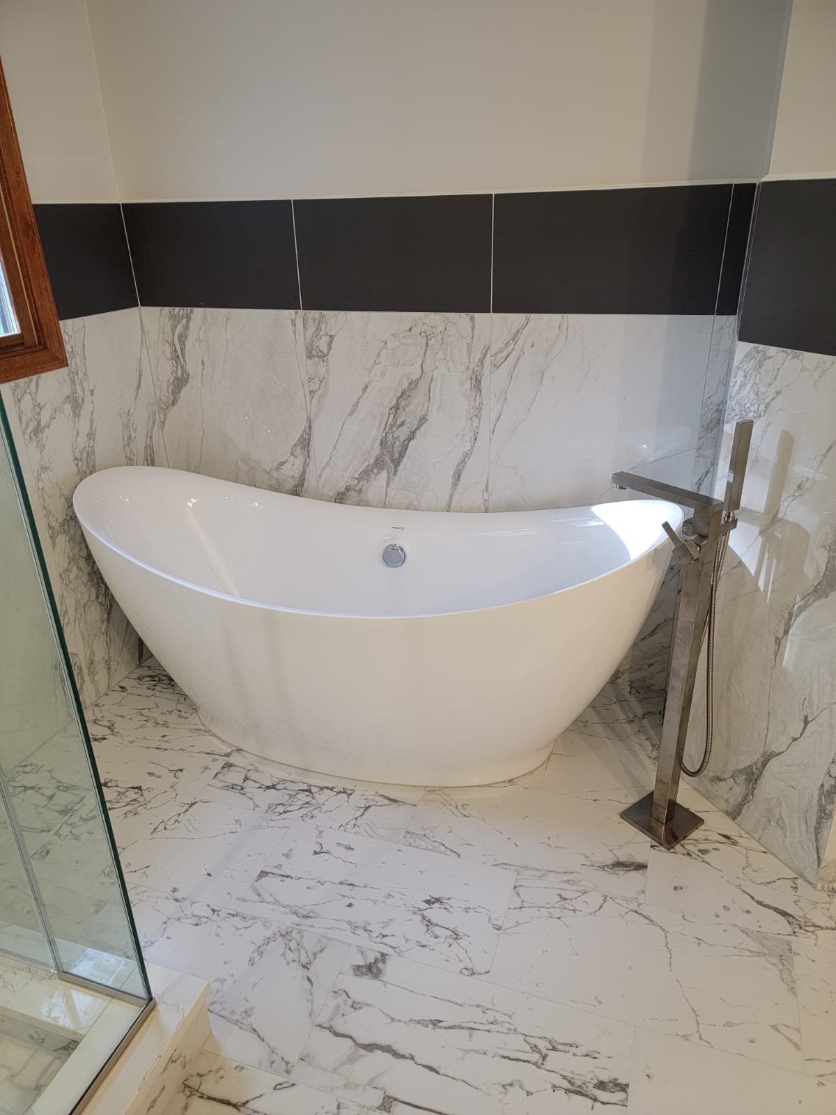 White, oval bathtub in marble-tiled bathroom. Chrome faucet stands beside it.
