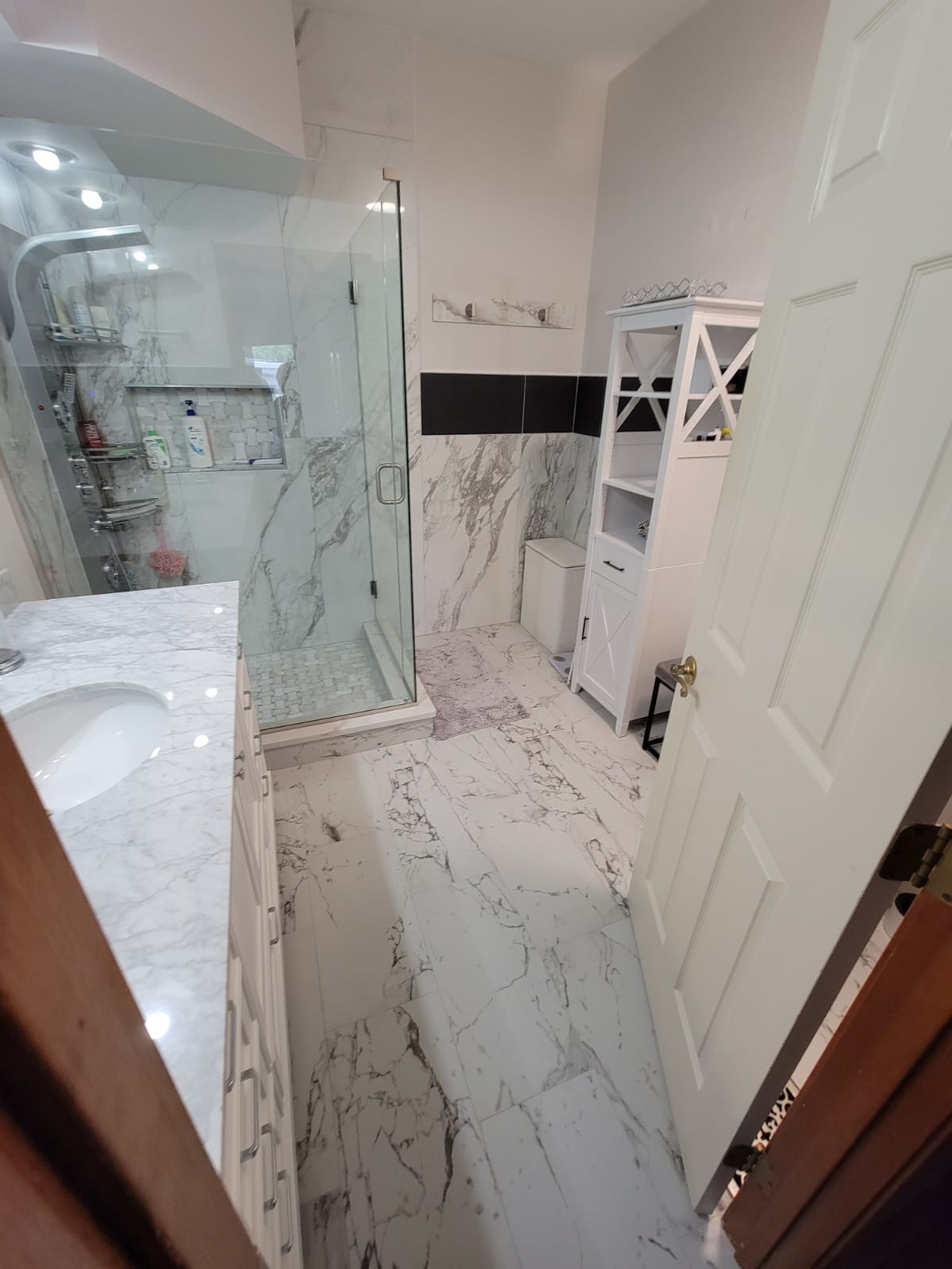 Bathroom with marble tile floors, glass shower, white cabinet, and a partially open white door.