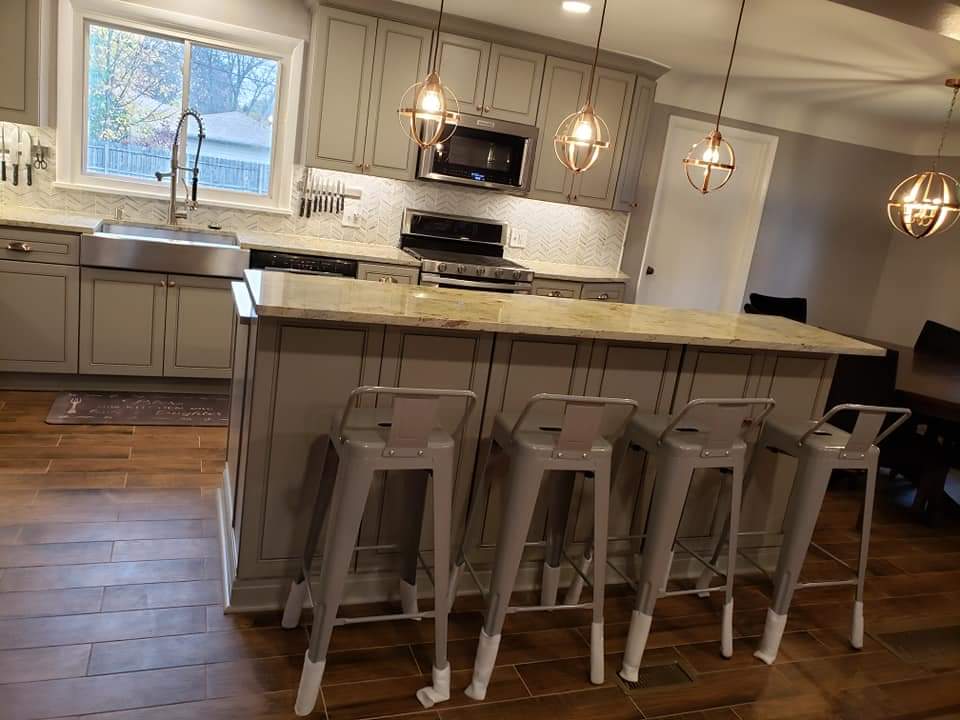 Modern kitchen with grey cabinets, light countertops, and metal bar stools at a central island.