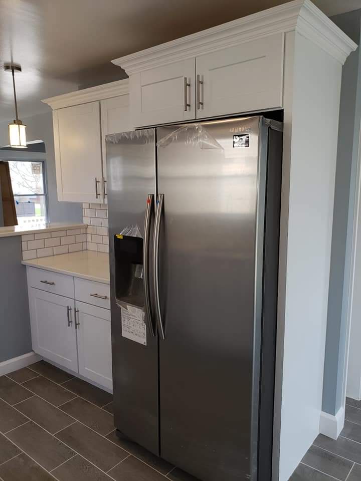 Stainless steel refrigerator next to white cabinets in a kitchen.