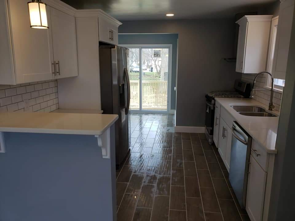 Modern kitchen with white cabinets, stainless steel appliances, and gray walls. Sliding glass door opens to a deck.