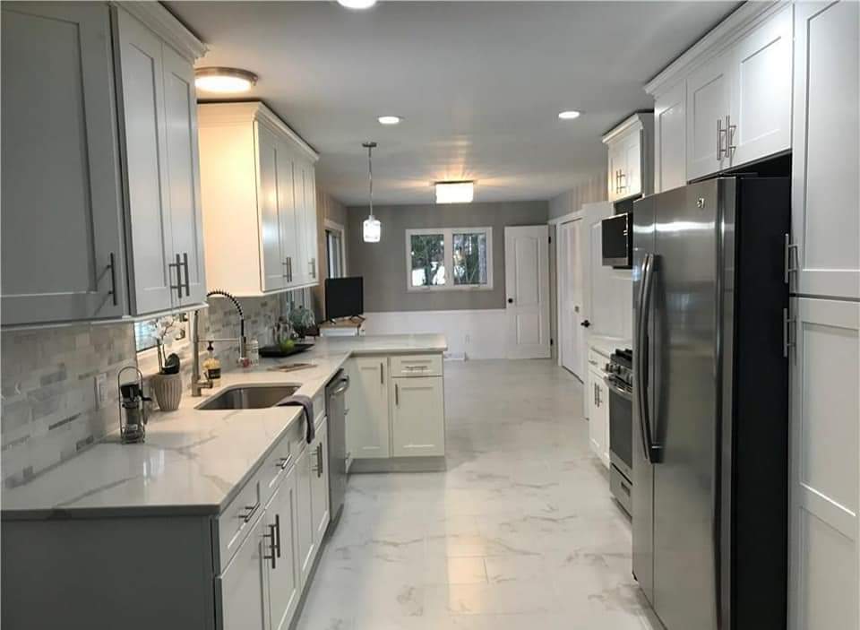 Bright, modern kitchen with white cabinets, marble countertops, stainless steel appliances, and tile floor.