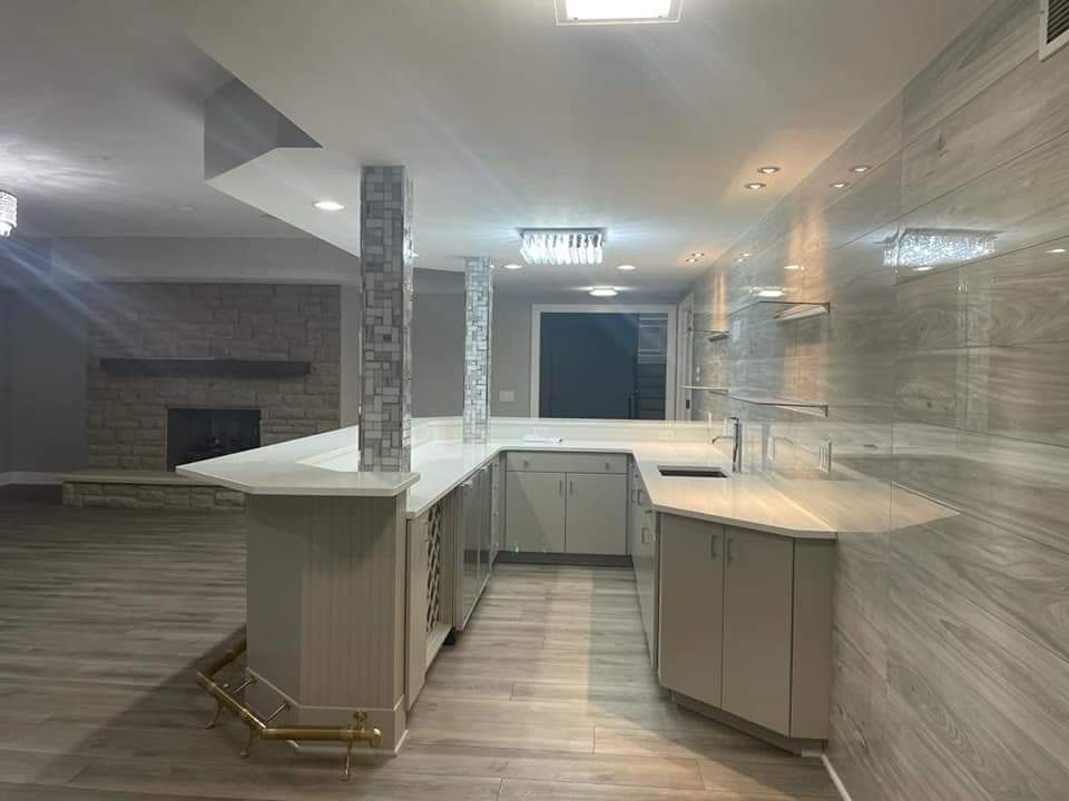 Finished basement with a bar, grey cabinets, white countertops, and stone-look tile walls.