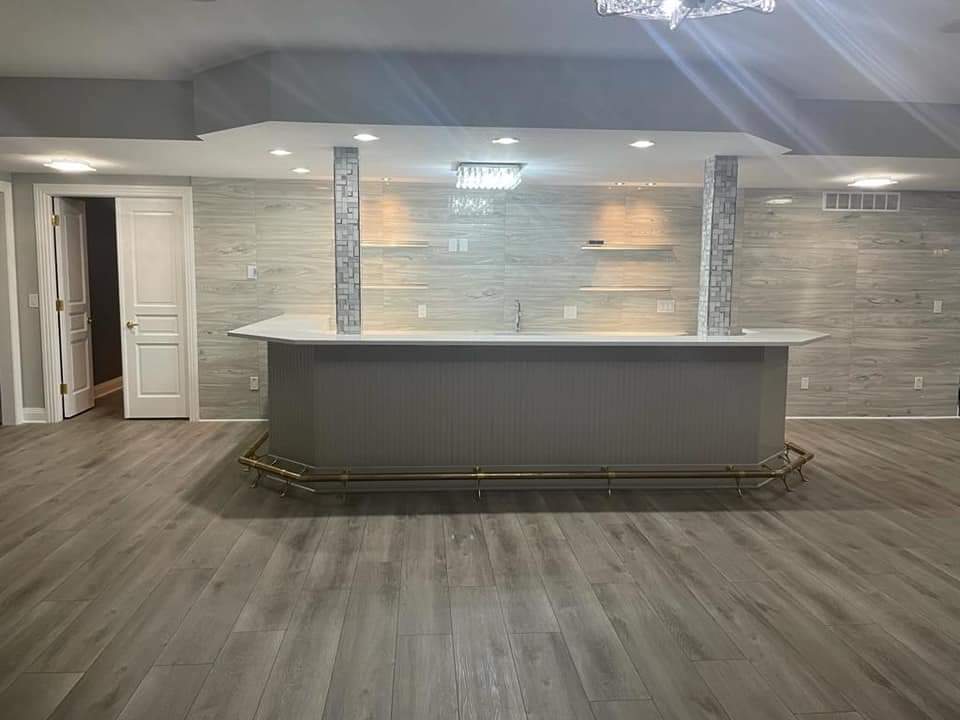 Finished basement with a bar; grey walls, wood flooring, brass foot rail.