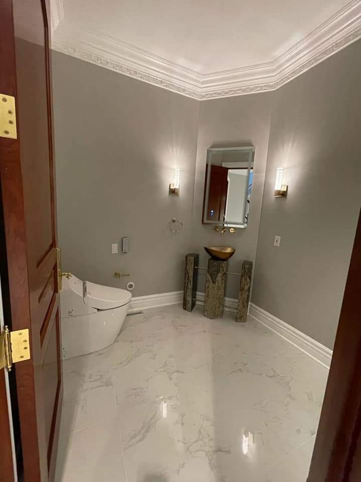 A small, elegant powder room with a marble floor, toilet, sink, and mirror; gold accents.