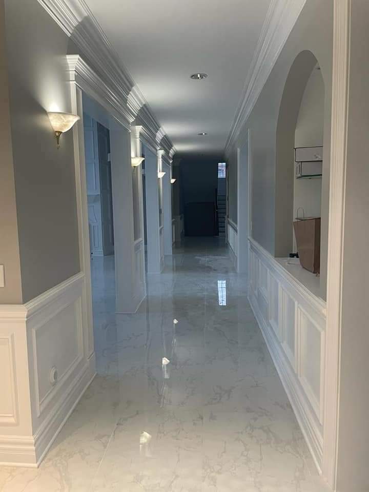Long, bright hallway with white molding, sconce lighting, and shiny tile flooring.