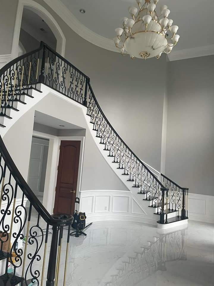 Grand, curved staircase with black and gold railing, white steps, and a large chandelier.