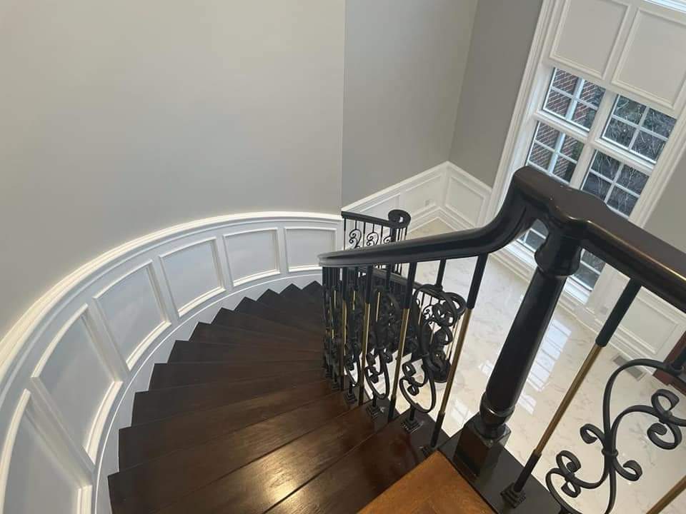 Dark wood spiral staircase with ornate black and gold railing, leading down from a windowed landing.